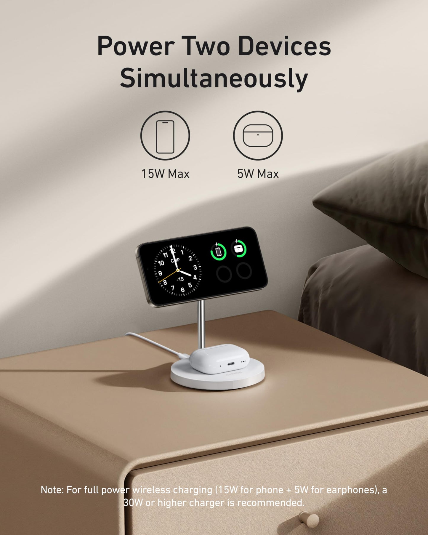 The Anker MagGo Wireless Charger (2-in-1 Stand) BOA by Anker charges your phone at 15W and earbuds at 5W simultaneously on your nightstand. Text: “Power Two Devices Simultaneously.” A bed and pillow are nearby.