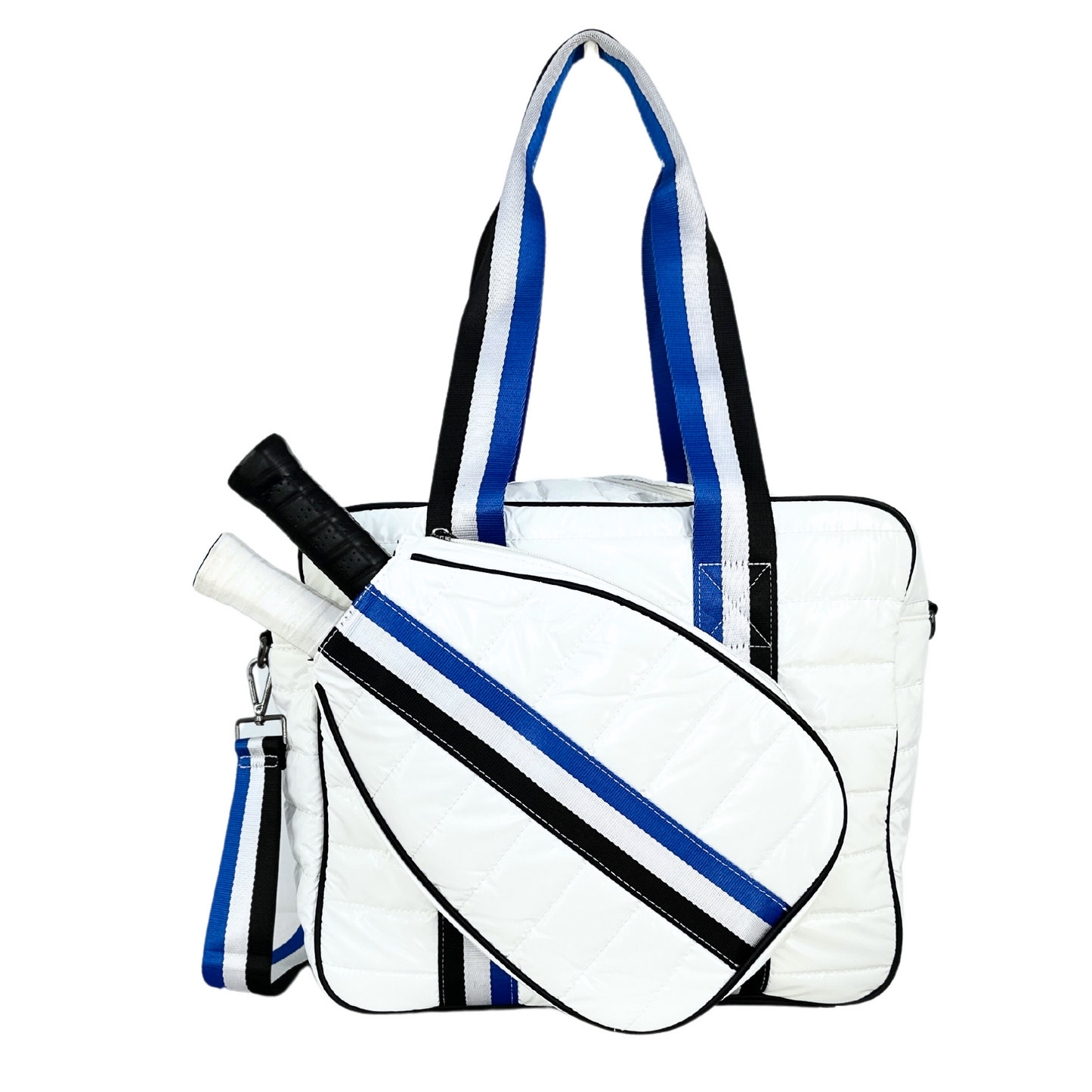 The Queen of the Court Kelsey Pickleball Bag is a white quilted tote with wide blue, black, and white striped handles and strap, plus a matching paddle cover holding two paddles—perfect as a stylish ladies’ pickleball bag.