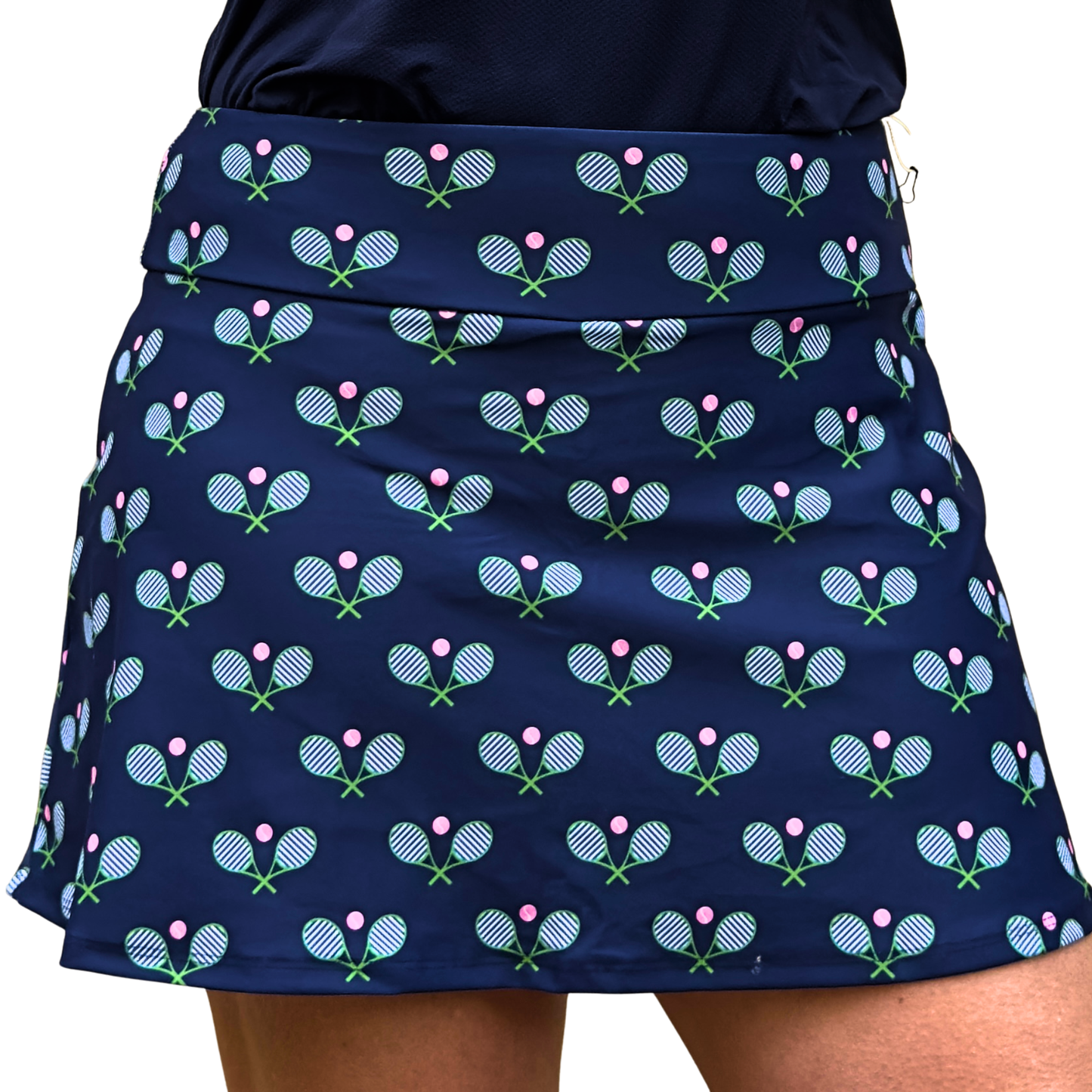 Wearing Queen of the Court's Stripey Tennis Navy skirt—made in the USA, this navy activewear features pink tennis balls and crossed rackets. The flared design shows only the torso and upper legs; the face isn’t visible.