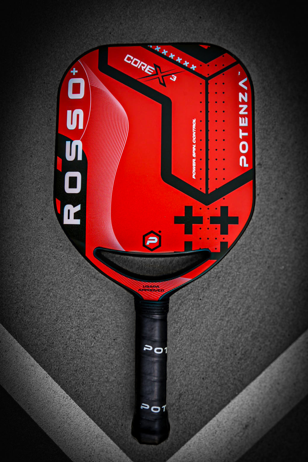 A Potenza Pickleball ROSSO+ COREx3 paddle in red and black lies centered on the court, crossing white boundary lines. It features bold graphics, textured patterns, a black handle with "POTENZA" in white, and COREx3 technology.