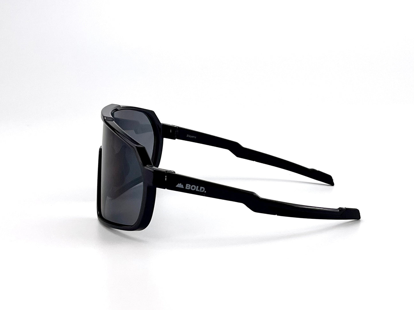 The BOLD Slayers Performance Sunglasses by boldouterwear feature an oversized black frame with dark lenses, shown side-on against a white background. The left arm displays “BOLD.” and a mountain logo in white.