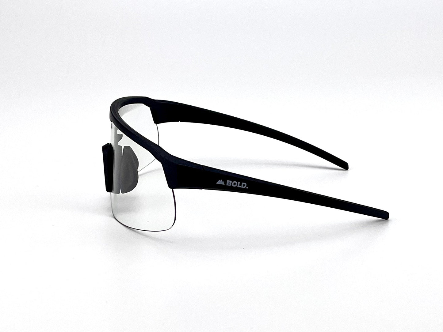 The BOLD Zippy Photochromic Sunglasses by boldouterwear are black half-rim performance eyewear with clear lenses, matte curved arms, adjustable nose pads, and “BOLD.” plus a mountain icon in white on the arm, set against a plain white background.