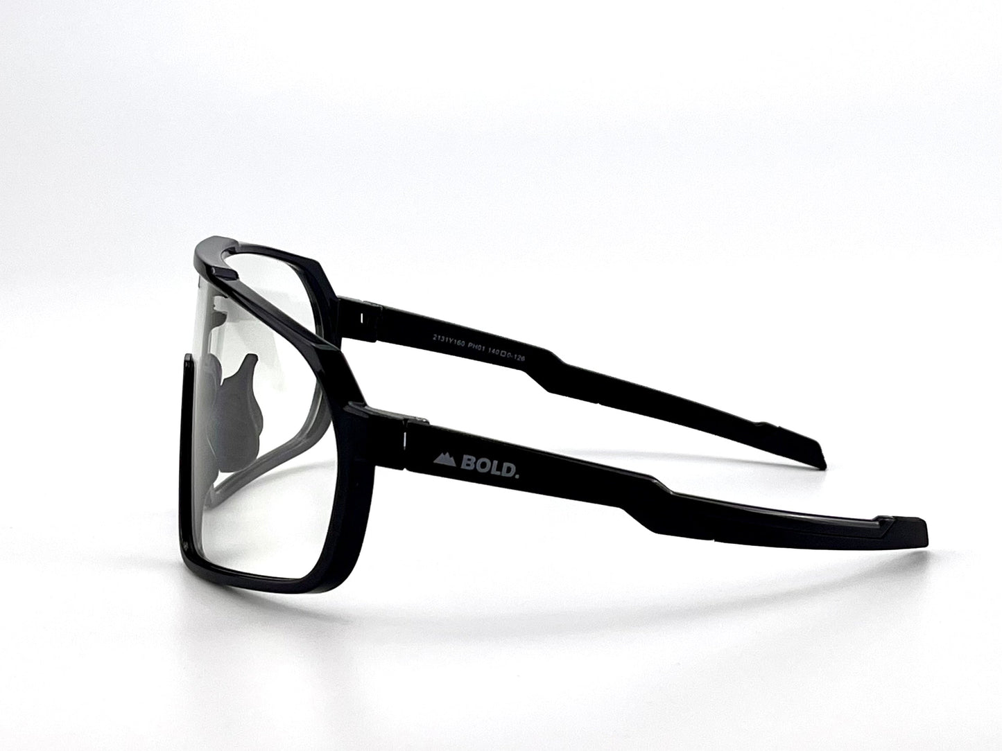 Shown in side view, the BOLD Slayers Photochromic Sunglasses by boldouterwear feature black oversized thick frames and light-adaptive clear lenses. "BOLD." and a mountain icon are printed in white on the temple arm against a plain background.