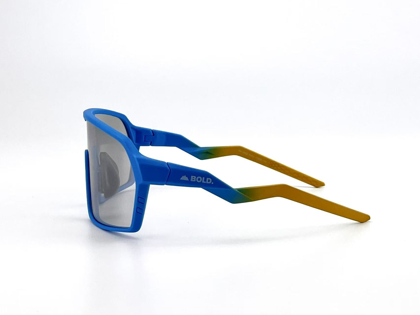 The BOLD Glow Photochromic Sunglasses by boldouterwear feature a blue front frame, gradient green-to-yellow arms (left arm with "BOLD." in white), and reflective, non-polarized lenses—ideal for MTB, ski & lifestyle. Shown on a plain white background.
