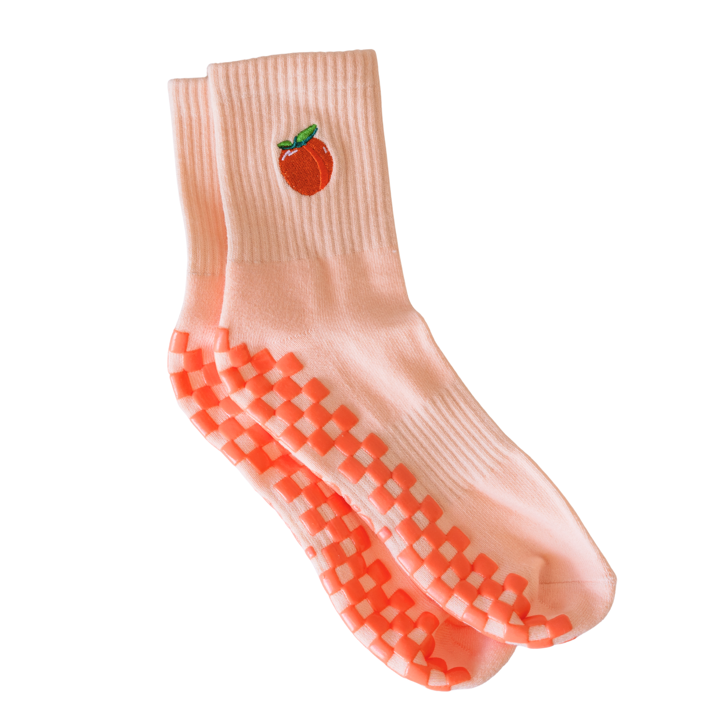 The Just Peachy Grip Sock by Revel features a light pink peach design with an embroidered fruit and green leaf, plus raised pink checkerboard grips on the soles—ideal cozy grip socks for Pilates. Shown neatly arranged on a white background.