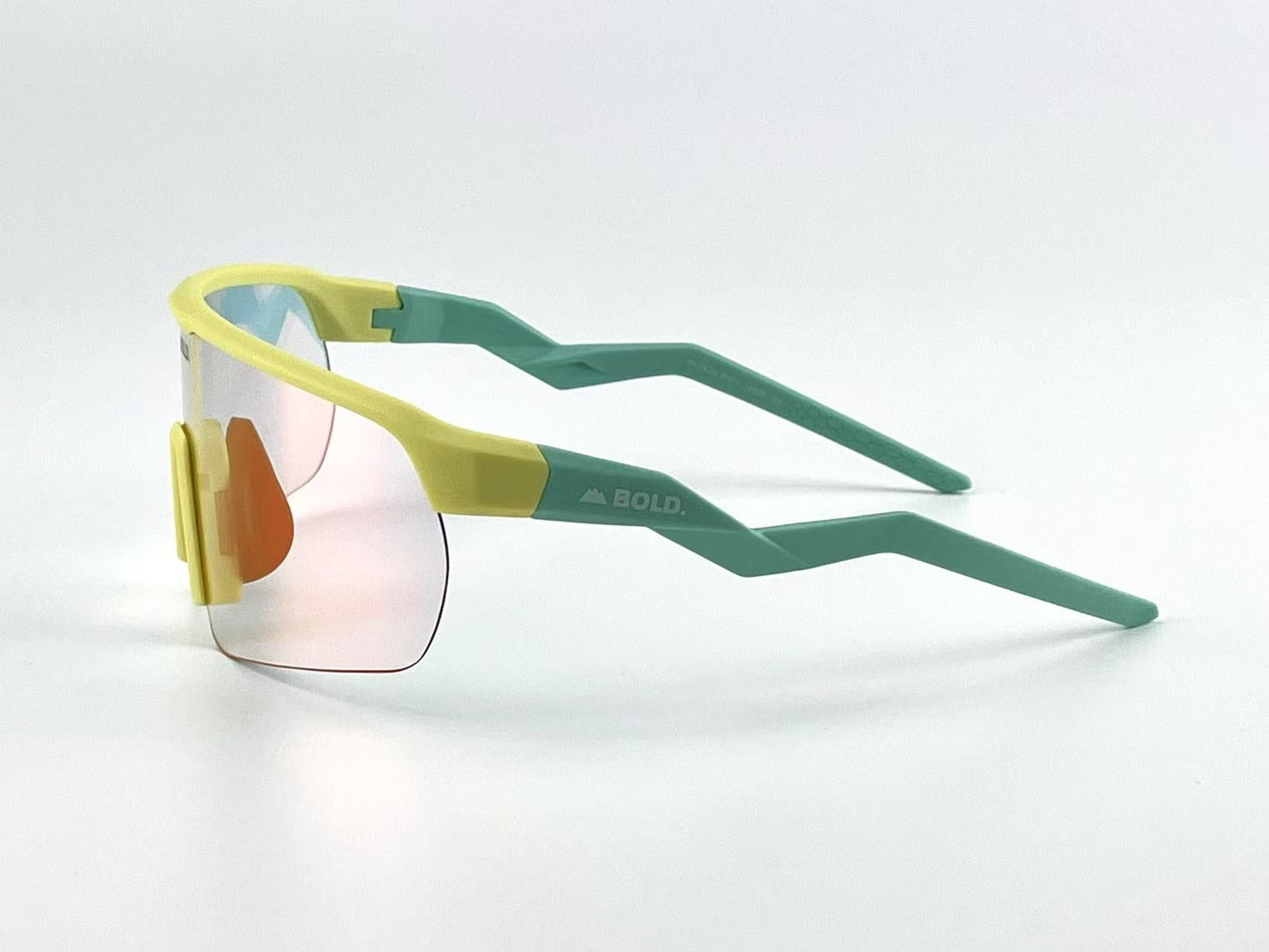 The BOLD Flash Photochromic Sunglasses by boldouterwear feature oversized pink lenses, a chunky yellow frame, and teal zigzag arms with “BOLD.” and a mountain logo. These light-adaptive shades are perfect for MTB, ski, or any adventure.