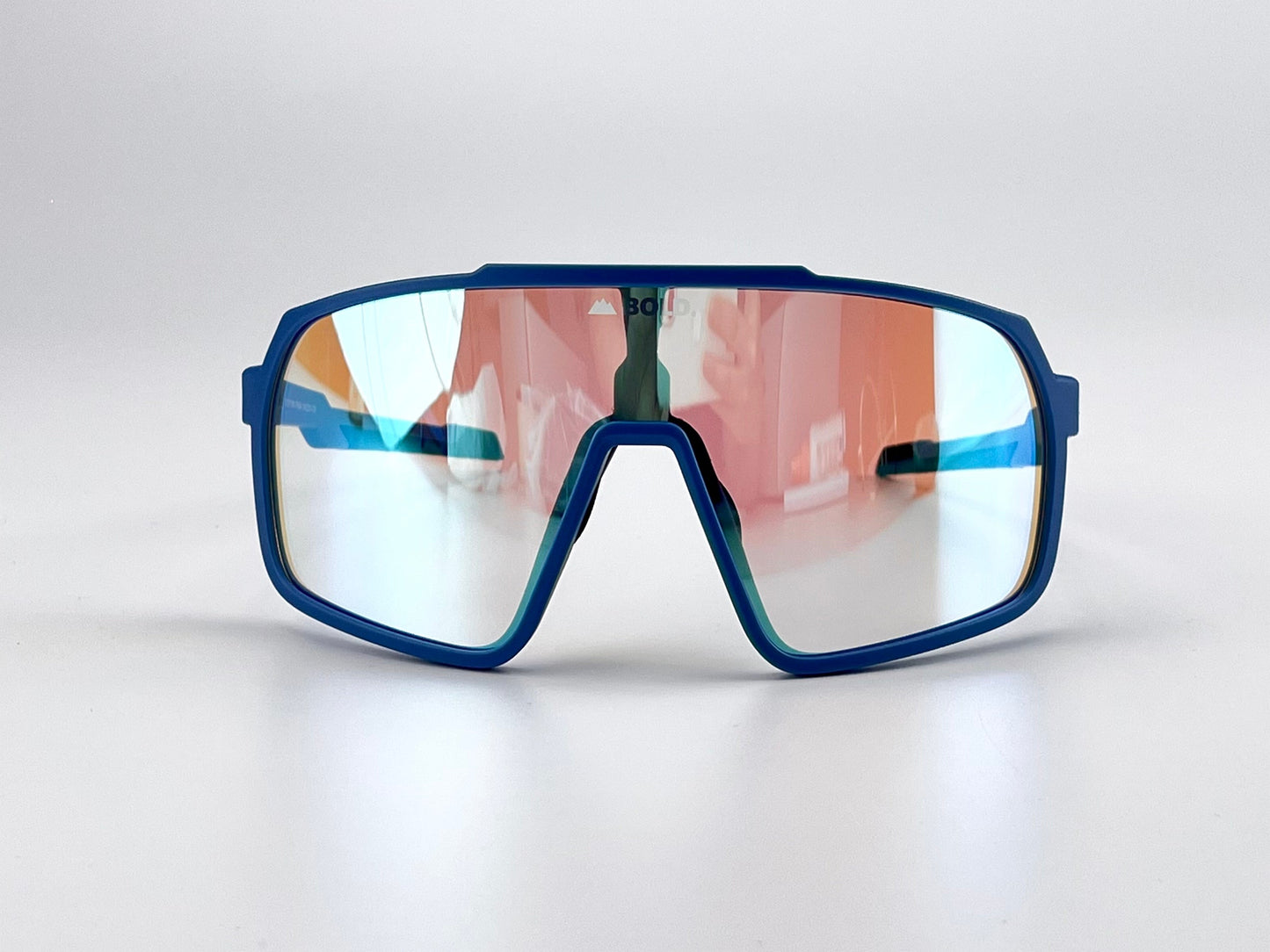 The BOLD Slayers Photochromic Sunglasses by boldouterwear feature sporty, oversized blue frames with geometric edges and large, light-adaptive mirrored lenses reflecting red and blue hues, shown on a plain white background.