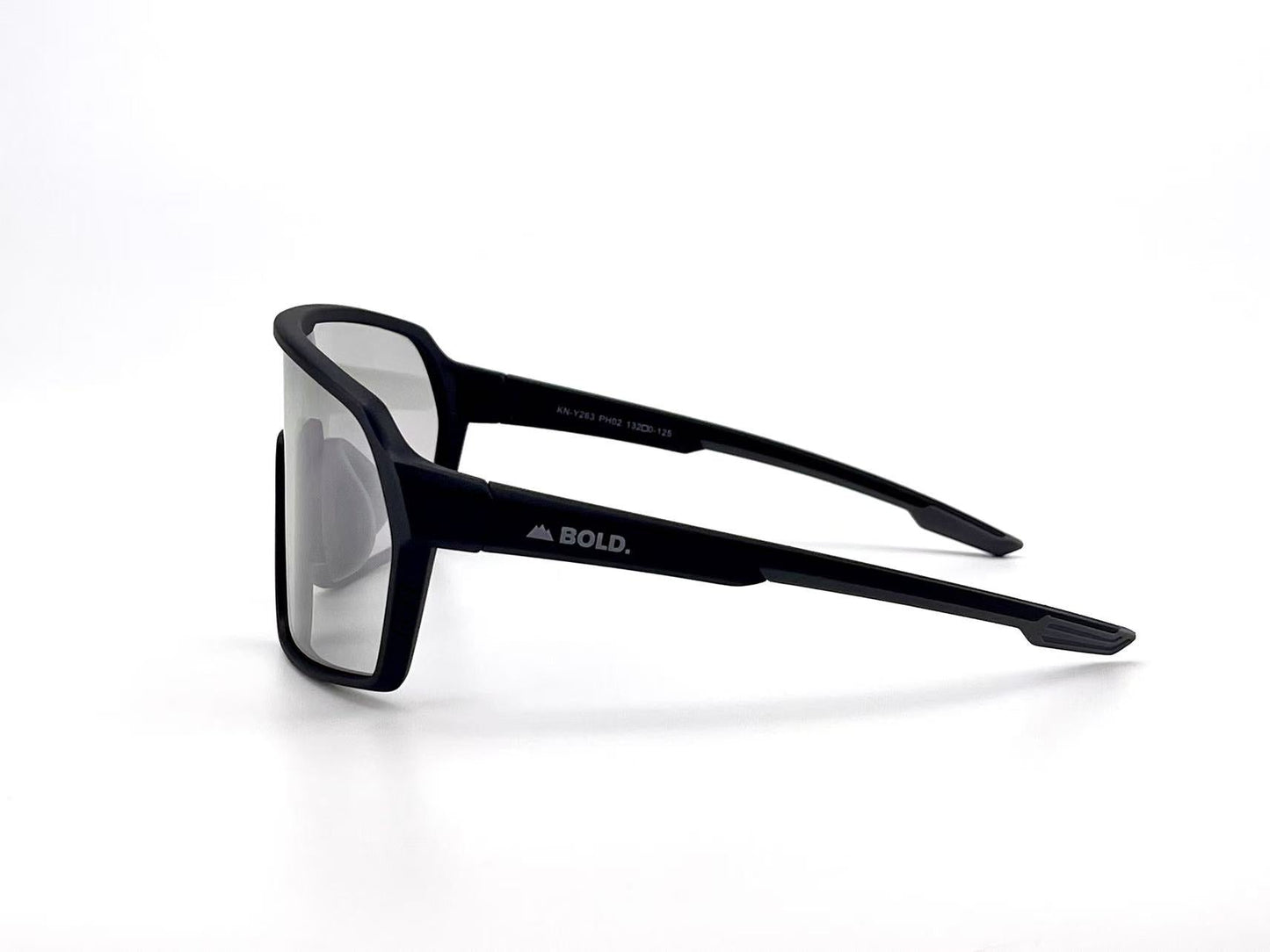 The BOLD Drift Photochromic Sunglasses by boldouterwear are shown from a side angle, featuring "BOLD." and a mountain graphic on the left temple. These black, rectangular frames with clear lenses combine modern style and versatile function.