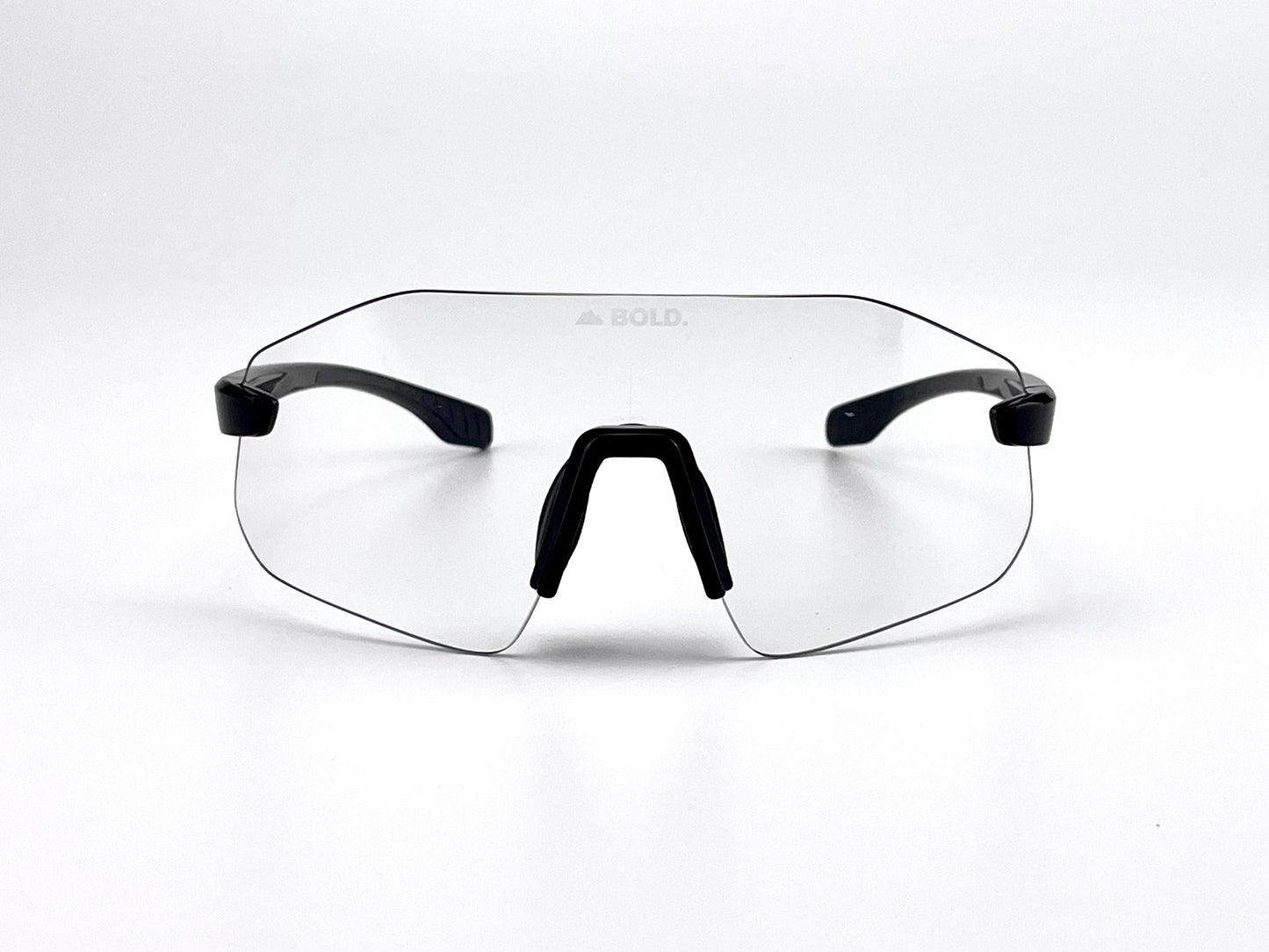 The BOLD Emerald Photochromic Sunglasses by boldouterwear feature frameless clear lenses, a black nose bridge, and black temple arms. "BOLD." is subtly printed at the top center of the lens against a white background. Ideal for MTB, ski & lifestyle wear.