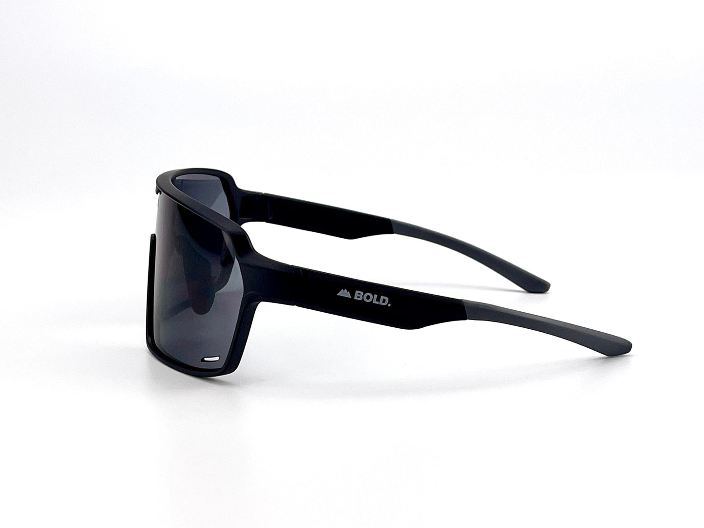 The BOLD Shadows Performance Sunglasses by boldouterwear feature a black wraparound frame with dark fixed-tint lenses, shown side view on white. The thick, angular design displays the white BOLD. logo and mountain icon near the hinge.