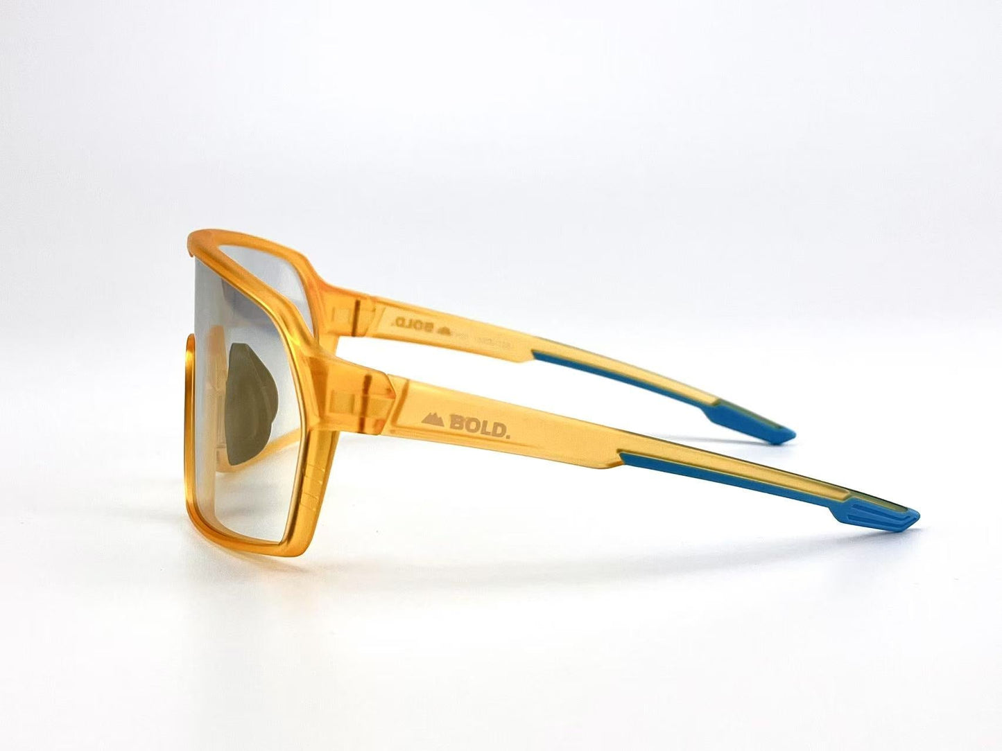 BOLD Drift Photochromic Sunglasses by boldouterwear feature translucent orange frames, rectangular yellow-tinted lenses, blue-tipped temples, and a “BOLD.” logo, shown in a three-quarter side view on a white background.