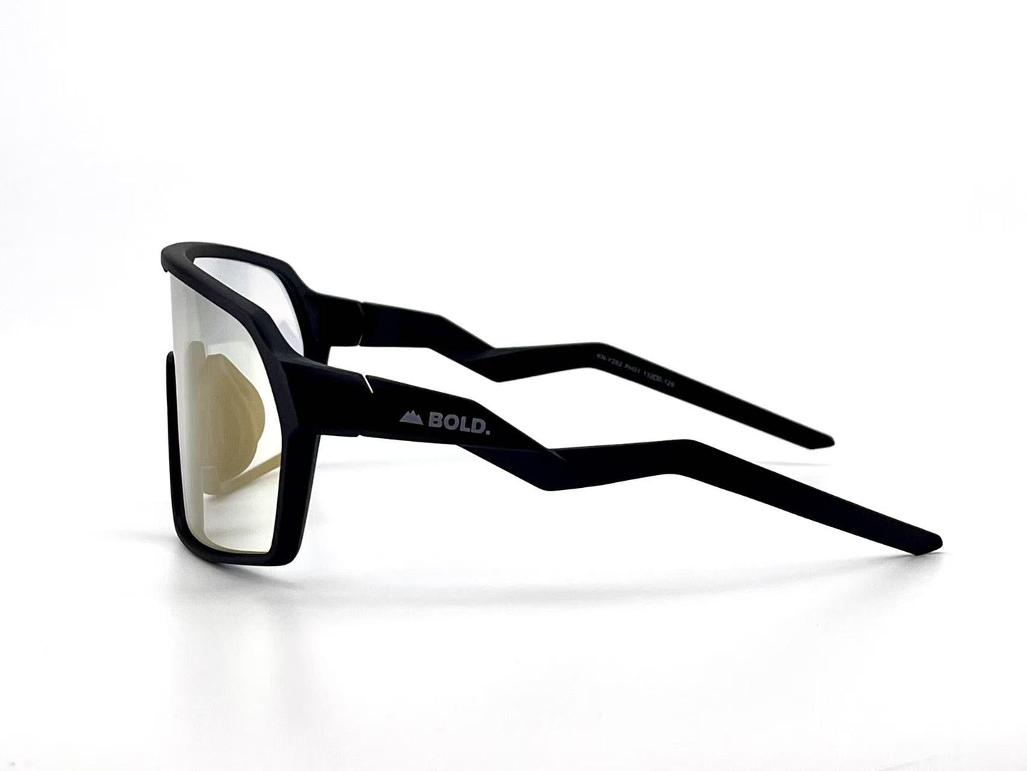 The BOLD Glow Photochromic Sunglasses by boldouterwear feature black, angular frames with zig-zag temple arms, lightly tinted non-polarized lenses, a matte finish, and a small white BOLD. logo on the left temple. Shown on a white background.