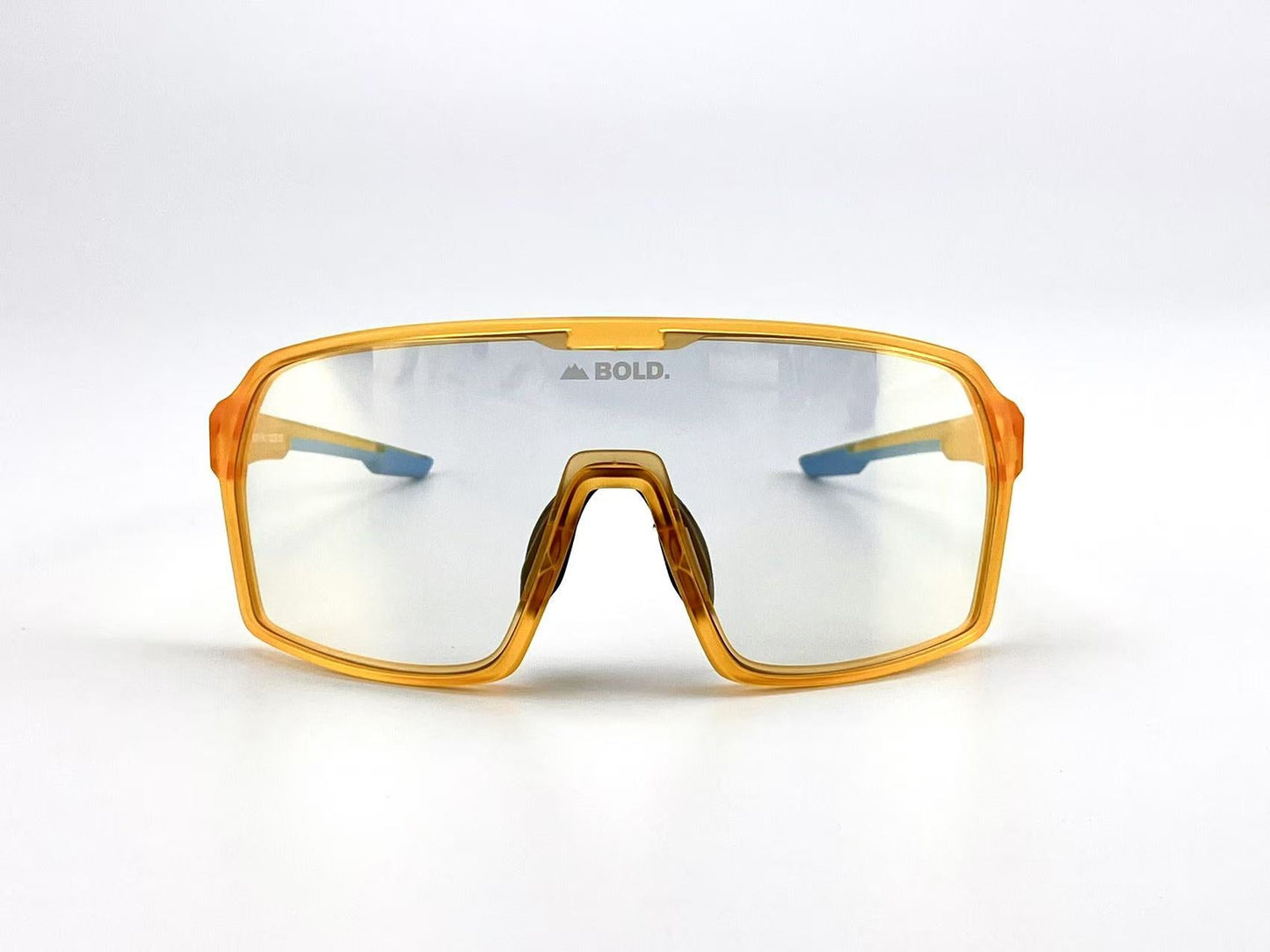The BOLD Drift Photochromic Sunglasses by boldouterwear feature a translucent orange wraparound frame, clear lenses with "BOLD." in gray on the center, and blue temple tips. Ideal for MTB, ski, and lifestyle use. Plain white background.