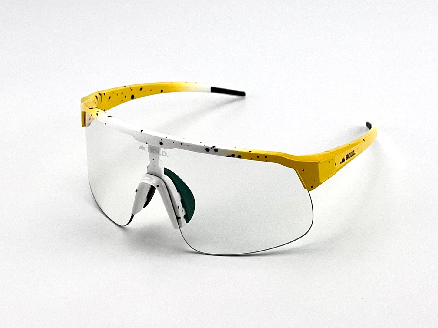 The BOLD Zippy Photochromic Sunglasses by boldouterwear feature a sporty white frame with yellow, black-speckled arms, green nose pad, and black arm tips—perfect for MTB, ski, or lifestyle use with clear wraparound lenses.
