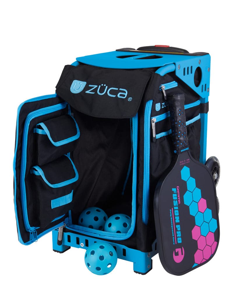 The ZUCA Pickleball Sport Black/Blue bag features large wheels, a sturdy frame, an open front revealing storage pockets with three yellow pickleballs inside, and a black paddle with pink and blue hexagons attached to the side.