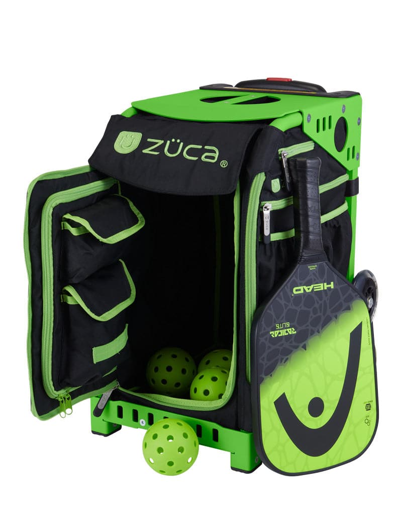 A ZUCA Pickleball Sport Black/Green rolling bag is open, showing several compartments. Three yellow-green pickleballs are inside and on the ground. A matching black and green pickleball paddle is attached to the side of the bag.