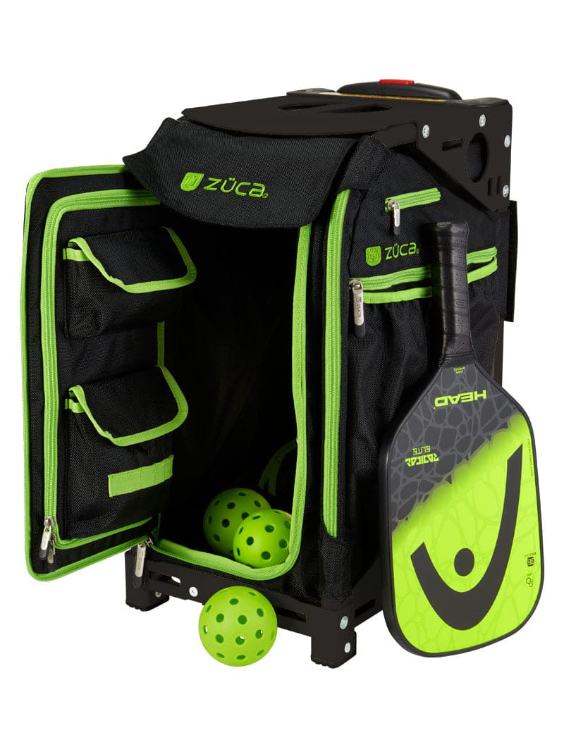 The ZUCA Pickleball Pro Black/Green rolling bag sits open, showing multiple compartments with three yellow pickleballs inside. A green and black HEAD paddle leans against the bag, which features zippered pockets and sturdy side wheels.