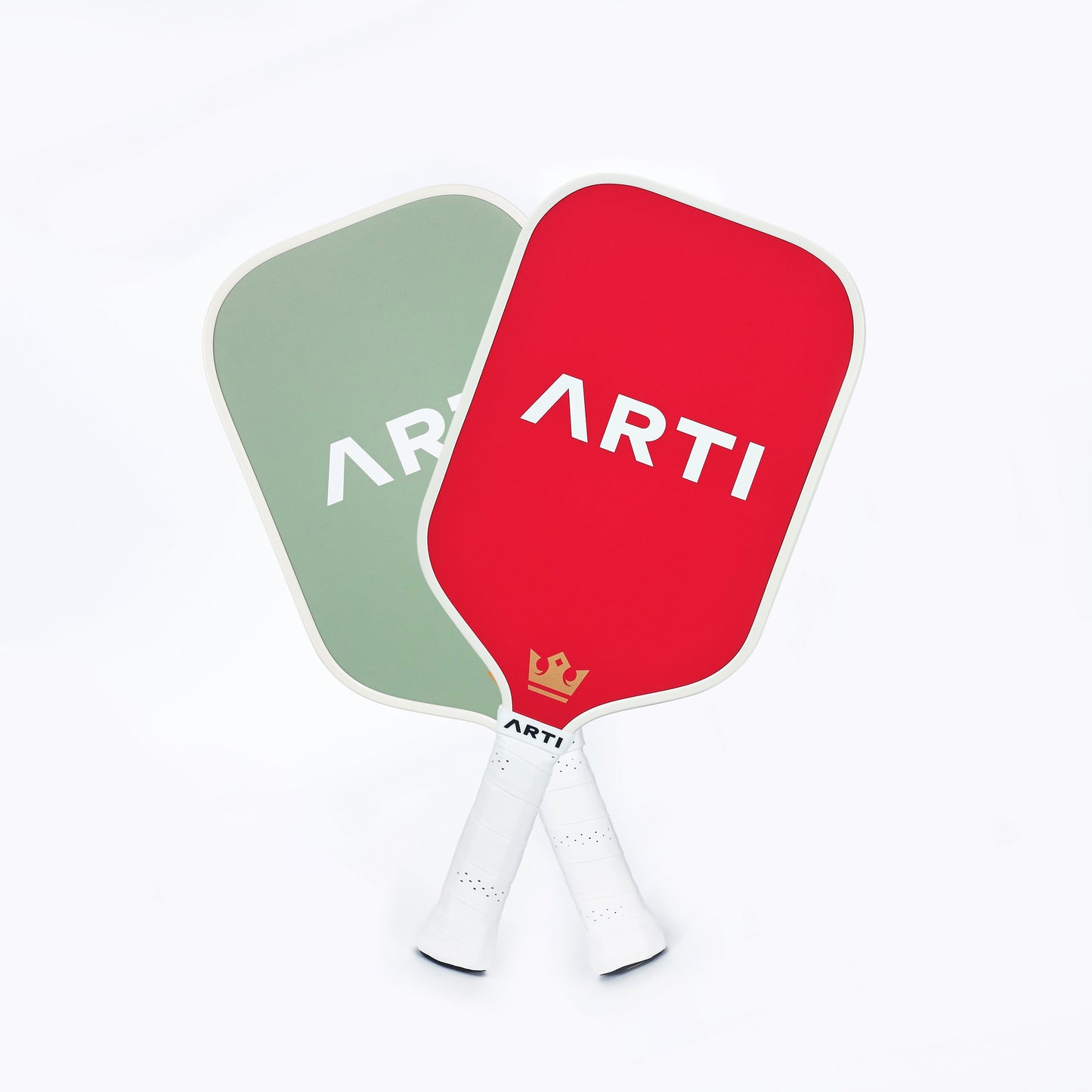 Two ARTI Fiberglass "Christmas Edition" pickleball paddles with white handles overlap on a white background—one light green, one red with a gold crown by the handle. Both have bold white ARTI branding. Brand: ARTI.