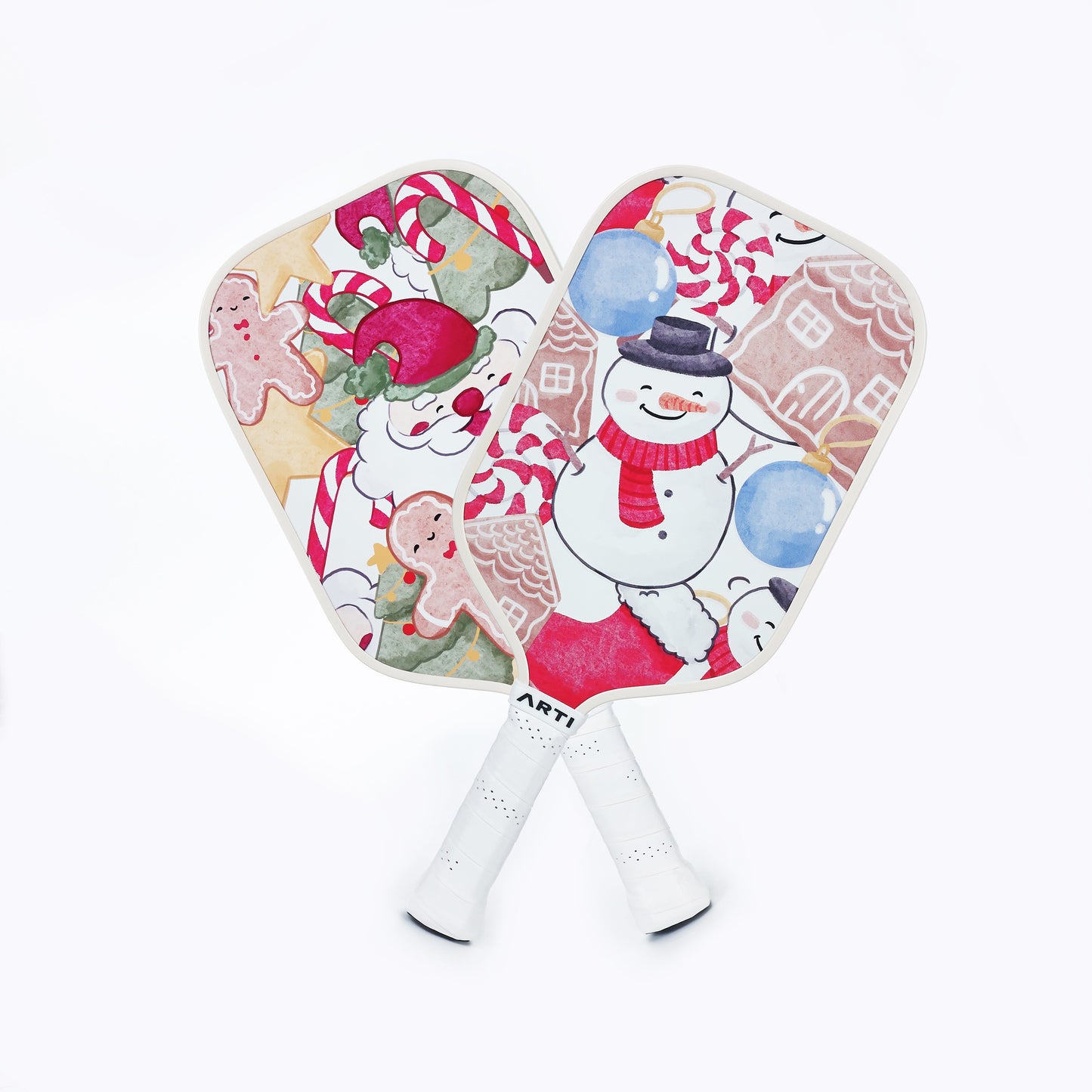 The ARTI Fiberglass "Christmas Edition" Pickleball Paddle set features two festive paddles—one with Santa, candy canes, and gingerbread cookies; the other with a snowman and blue ornaments. Both have white handles and are crossed at the base.