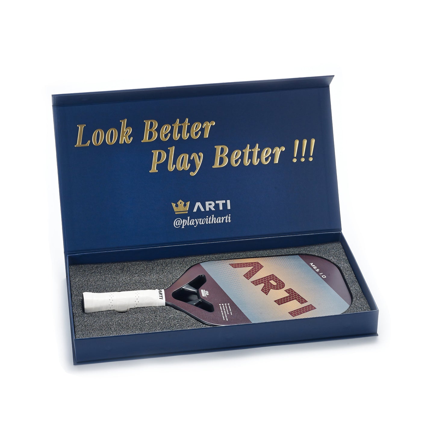 A blue box with gold “Look Better Play Better!!!”, the ARTI logo, and a crown contains the USAPA-approved ARTI Carbon Fiber "MASTERY ELITE 1.0" paddle with white grip, set in black foam; lid and handle show @playwitharti.
