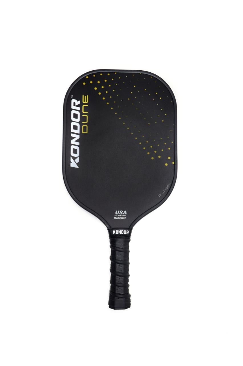 A black DUNE 3K Carbon Pickleball Paddle by KONDOR PICKLEBALL with "KONDOR DUNE" in white and yellow on the left, a textured EVA comfort grip, small yellow dots along the top right edge, and "USA Pickleball Approved" near the handle.