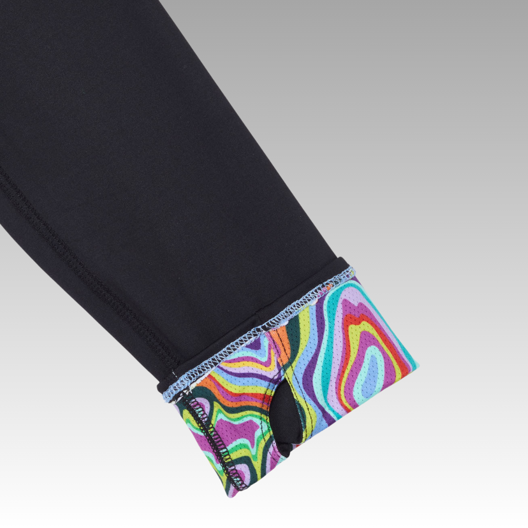 A close-up of the Playly Store Soleil Tech Shirt shows black fabric, a turned-up cuff with a colorful abstract pattern, thumbhole, and visible stitching. Made from breathable UV-protective material. Gray gradient background.