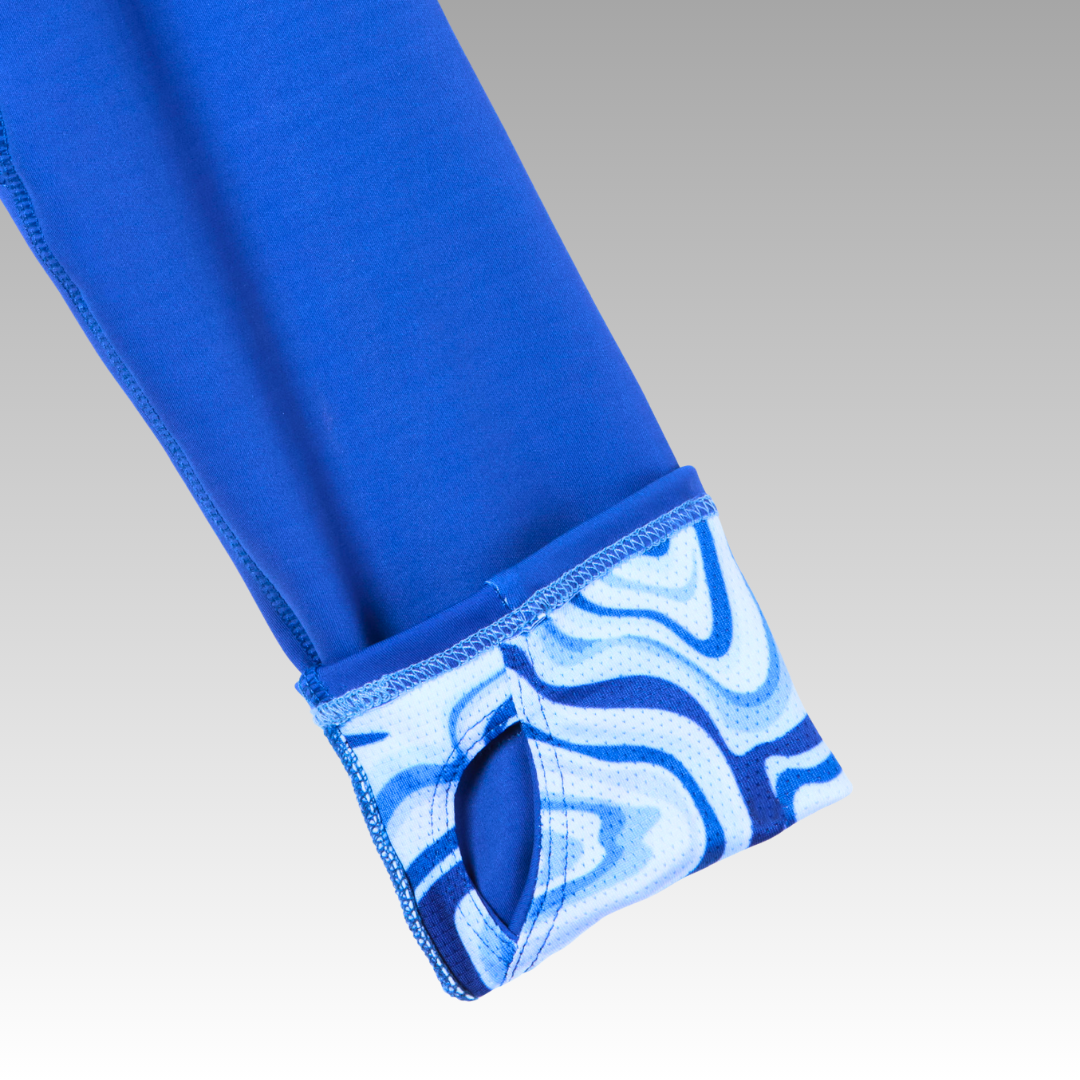 A close-up of the Soleil Tech Shirt by Playly Store shows a blue sleeve with a thumbhole cuff. The breathable cuff features a white and blue marble wave pattern, contrasting with the solid blue sleeve and gray background.