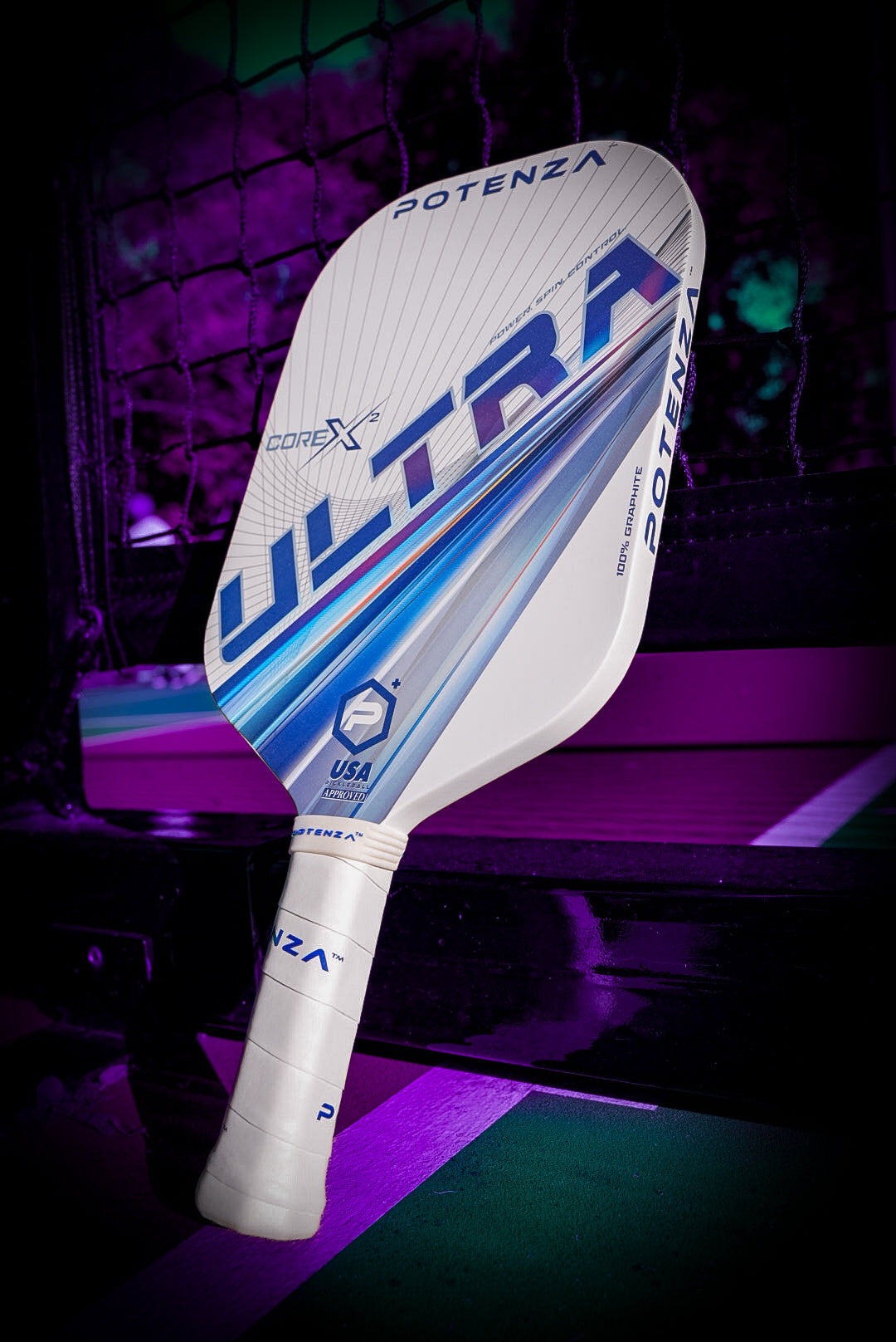 A white Potenza Pickleball ULTRA+ COREx2 edgeless paddle with blue, silver, and purple accents leans against a court net. The paddle, featuring POTENZA branding and a USA logo, stands out amid purple lighting and court lines.