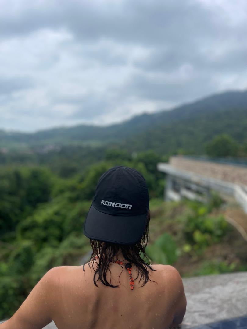 A woman in a KONDOR PICKLEBALL Game Day Ready Quik Dry Hat with an athletic brim gazes at a mountain range, ready for any adventure with advanced Quik-Dry technology.
