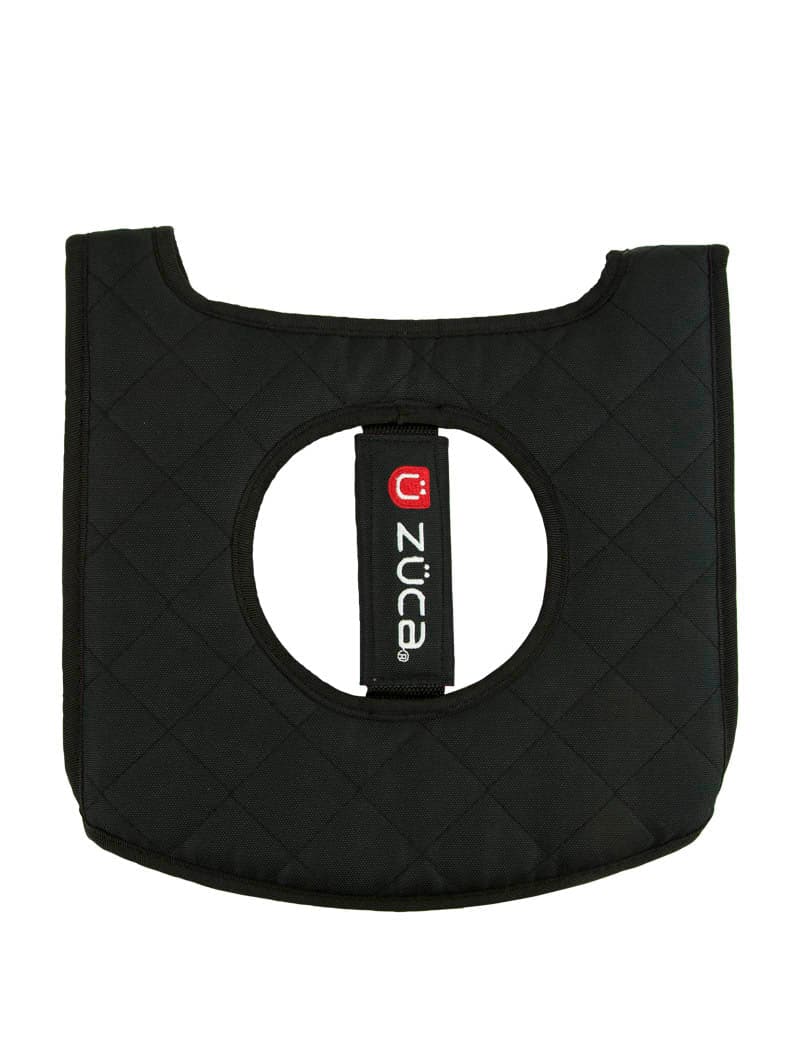 The ZUCA Reversible Seat Cushion is a black, quilted pad with a large central circular hole, padded edges, and a vertical white-red “züca” tag. It has a rectangular shape with slightly rounded bottom corners.