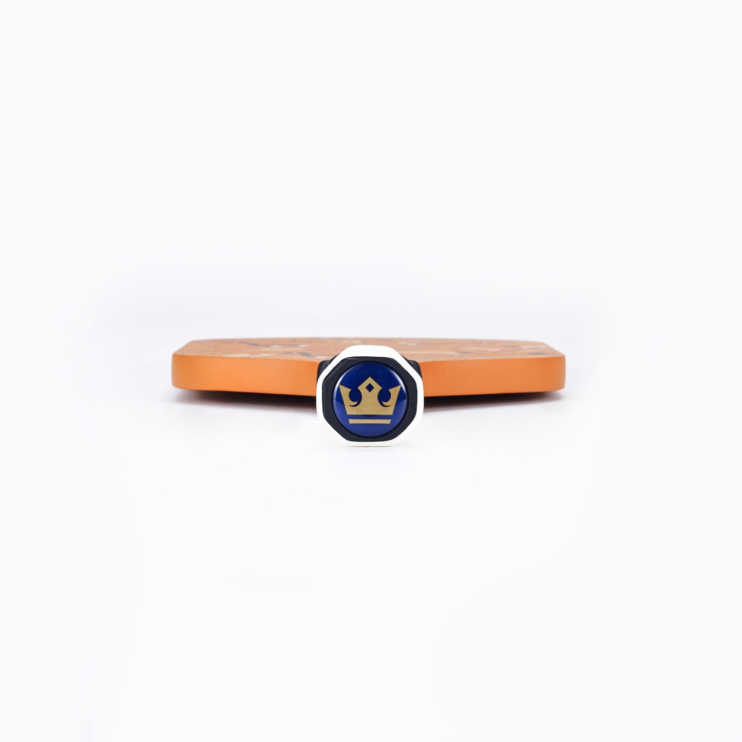The ARTI Carbon Fiber "TEXAS" Paddle by ARTI stands upright behind a small, round pin with a silver rim, blue center, and gold crown, both displayed against a plain white background.