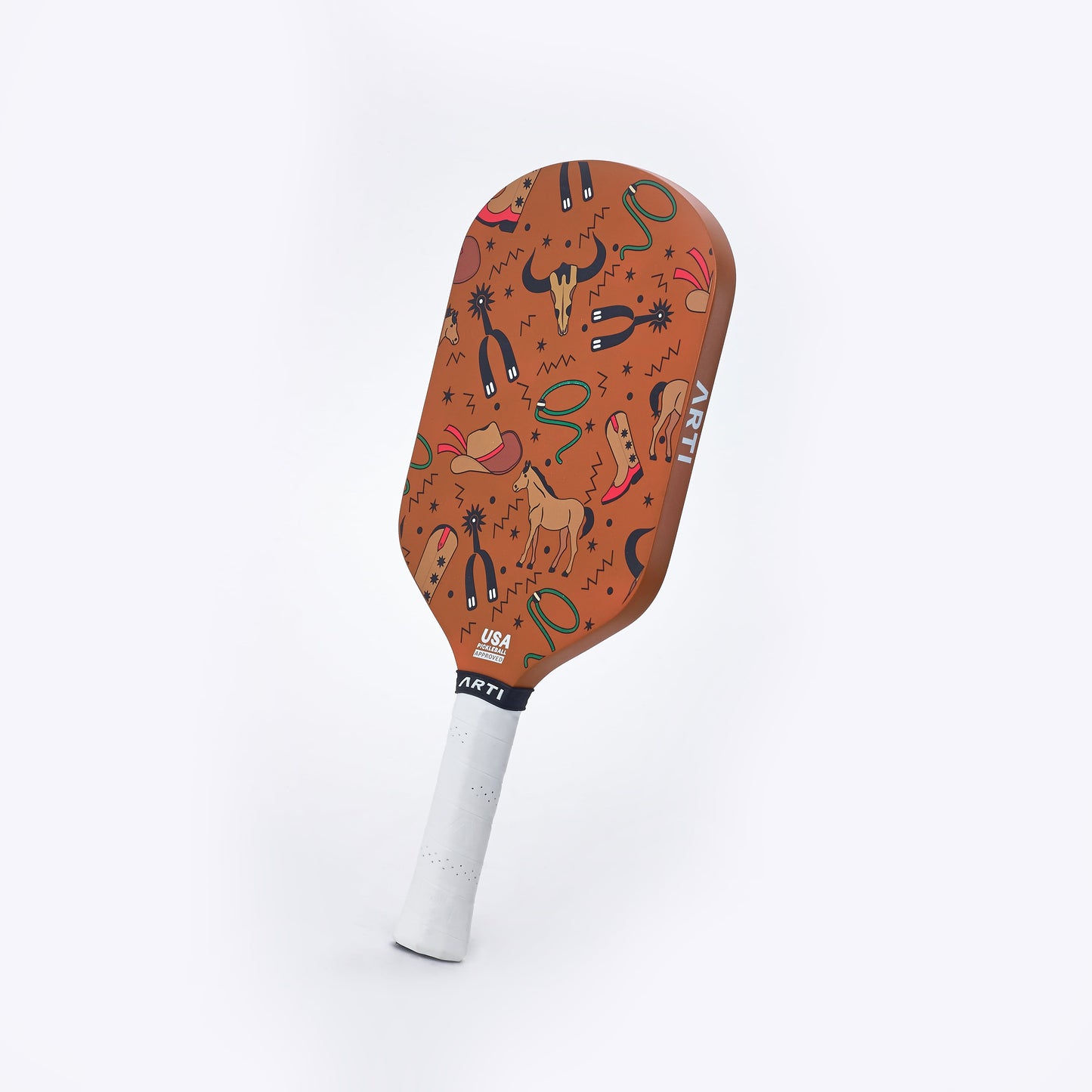 The ARTI Carbon Fiber "TEXAS" Paddle features a white grip and reddish-brown face with playful Western art—cowboy boots, hats, horses, cacti, and lassos. USAPA approved with ART and USA Pickleball text near the handle.