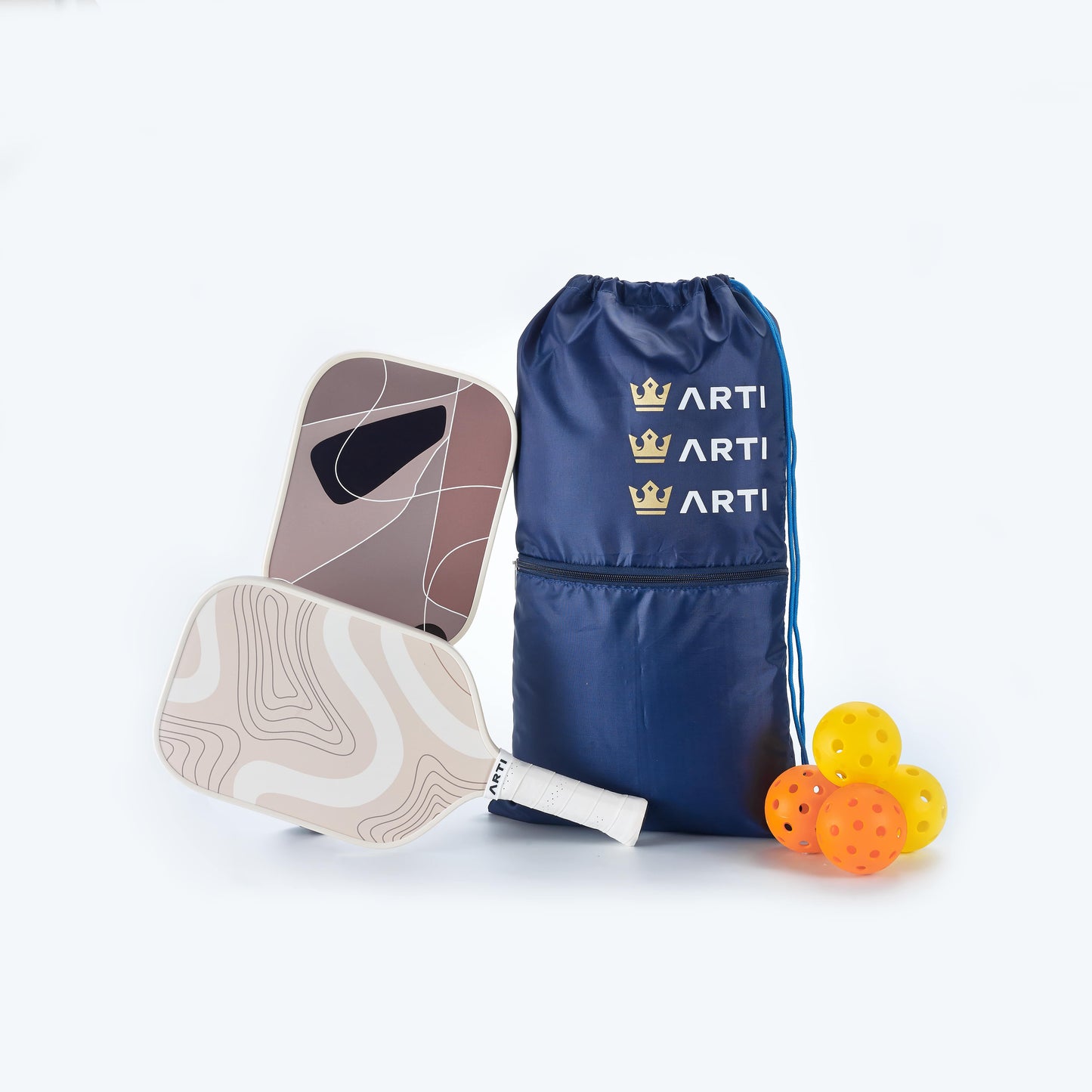 The ARTI Fiberglass "Sandstorm" Pickleball Paddle Set by ARTI includes two USAPA-approved paddles with honeycomb polymer cores, four yellow perforated balls, and a blue ARTI bag. One paddle has earthy tones; the other features geometric shapes.