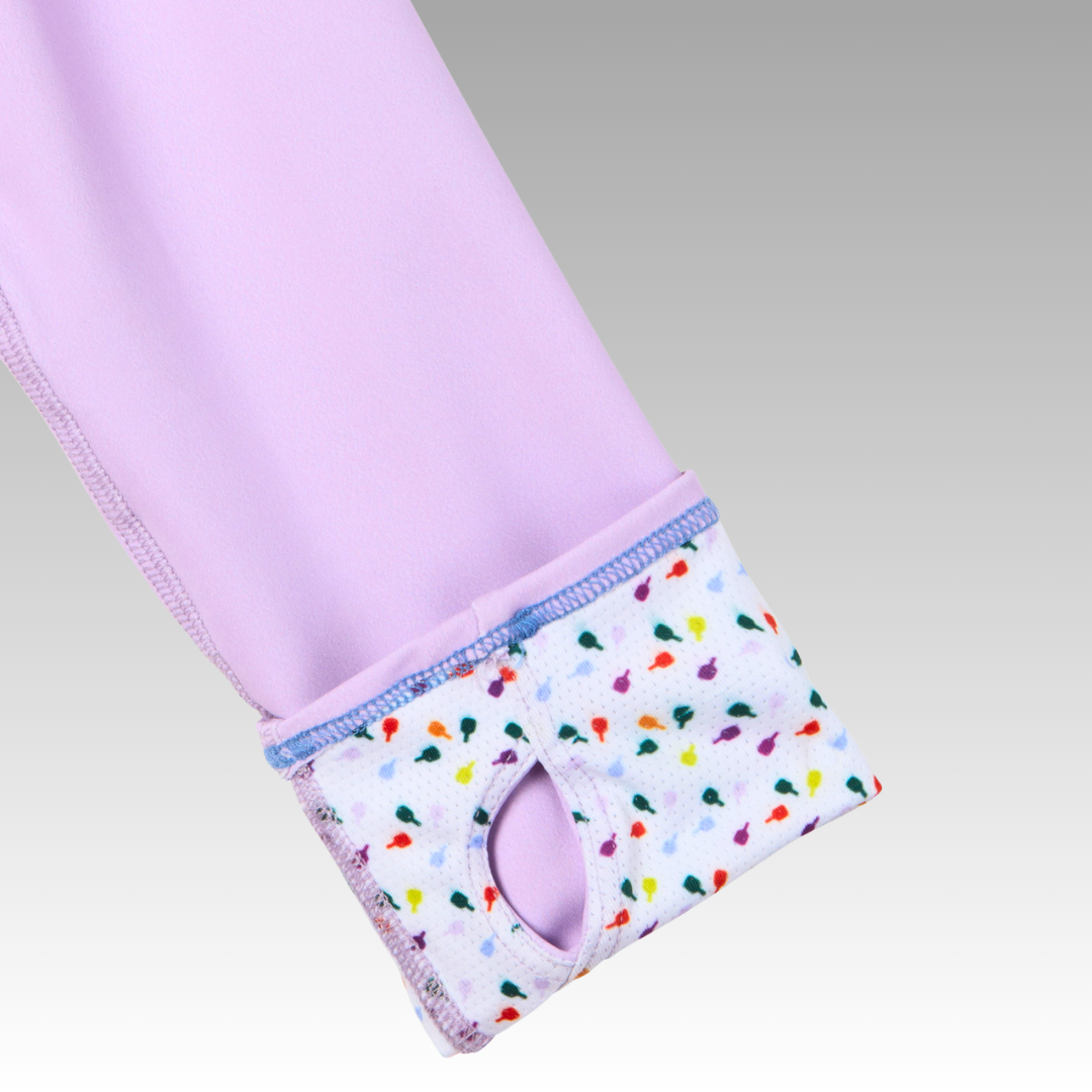 A close-up of the Soleil Tech Shirt by Playly Store shows its lavender long sleeves with white cuffs featuring a vibrant bird pattern, purple stitching, and thumb holes. The cuff is crafted from breathable fabric, set against a smooth gray gradient background.