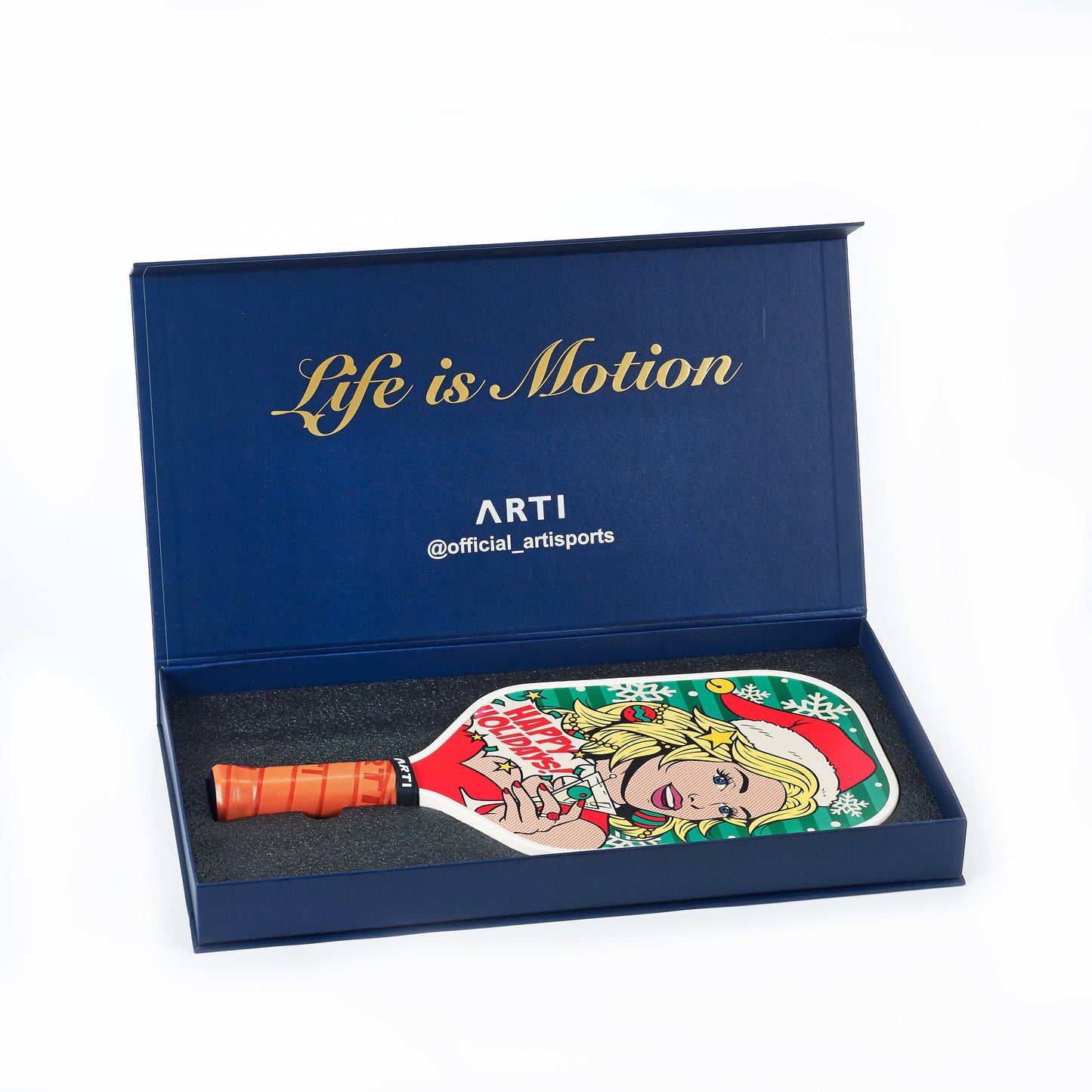 The ARTI Carbon Fiber Kristen&Kristy "Happy Holidays" Paddle, featuring a pop art blonde woman in a Santa hat, comes in a dark blue gift box with "Life is Motion" in gold and the ARTI logo plus their Instagram handle.