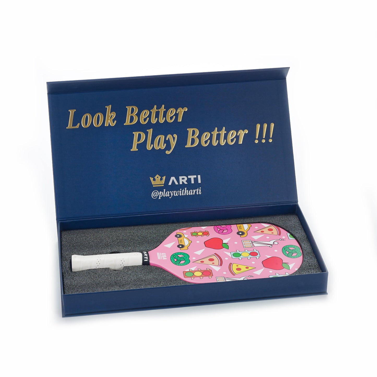 A blue box with gold text "Look Better Play Better !!!" and ARTI @playwitharti contains the ARTI Carbon Fiber "NEW YORK" Paddle, a USAPA approved pink racket with playful pizza, sunglasses, donuts and more, nestled in grey foam.