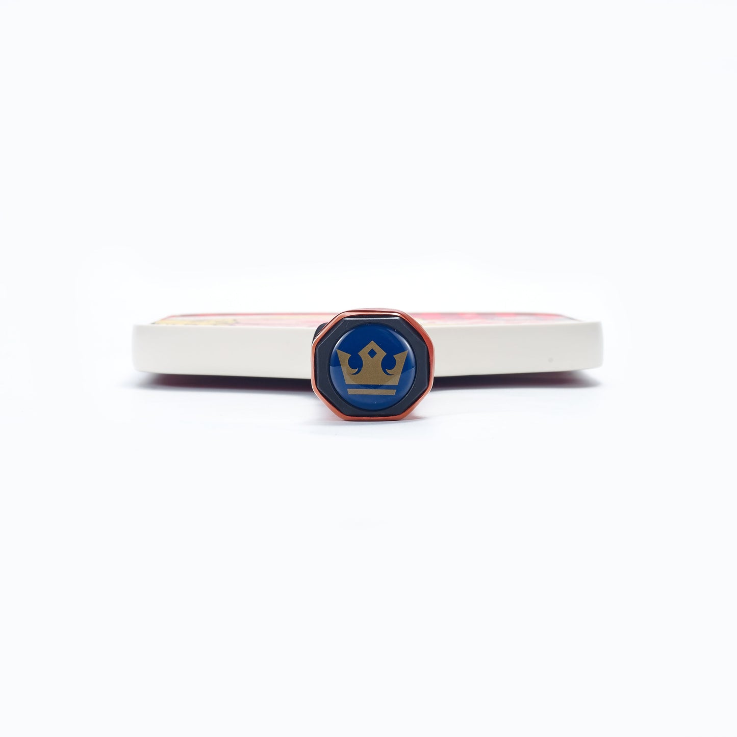 A close-up of an octagonal pin with a gold crown on blue stands upright before the ARTI Carbon Fiber Kristen&Kristy "X-MAS" Paddle by ARTI, featuring a red and white T700 carbon fiber surface, all set against a plain white background.