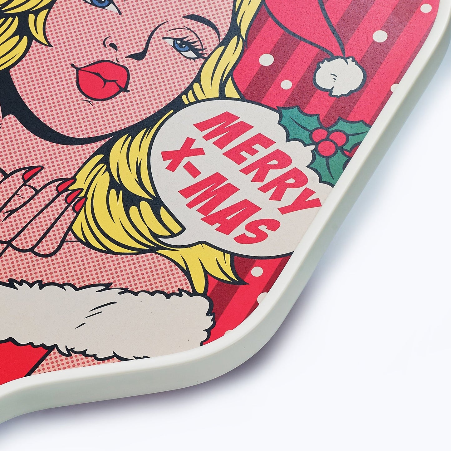 A pop art-style image of a blonde woman in a Santa outfit blows a kiss and holds the ARTI Carbon Fiber Kristen&Kristy "X-MAS" Paddle by ARTI. A speech bubble says MERRY X-MAS on a red background with white dots and green holly.