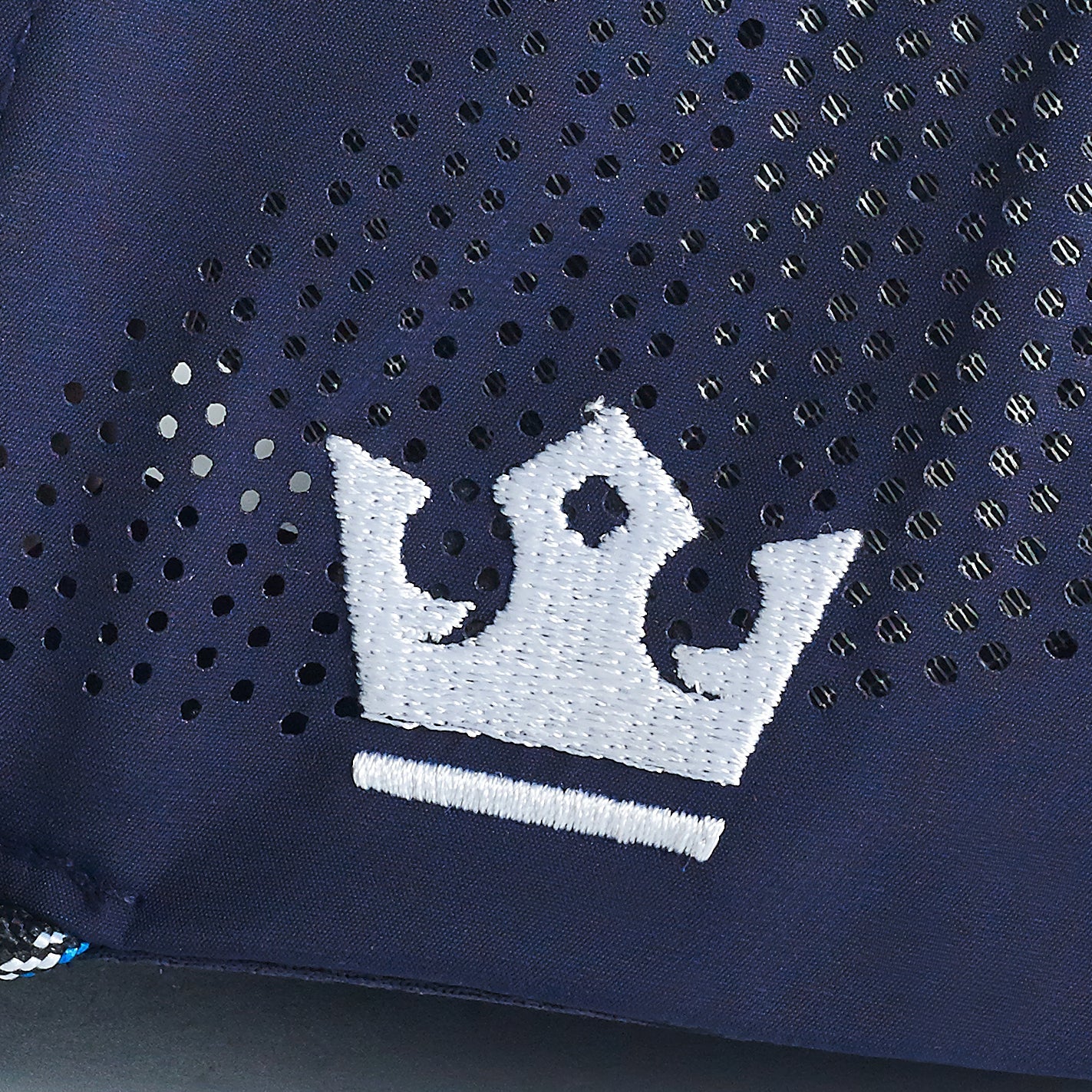 A close-up of the ARTI Navy Performance Rope Mesh Classic Hat shows its breathable mesh fabric with small perforated holes and a white, three-point crown logo with a line beneath it. The stitching and texture of this ARTI hat are clearly visible.