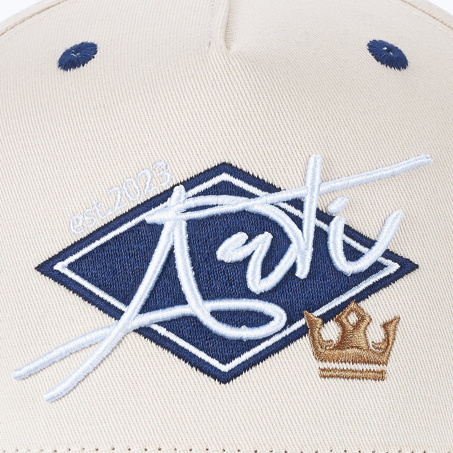 The ARTI Throwback Classic Rope Hat features a beige design, navy eyelets, and a blue diamond patch with stylized “ARTI” script and “est. 2023”, plus a gold embroidered crown for timeless style.