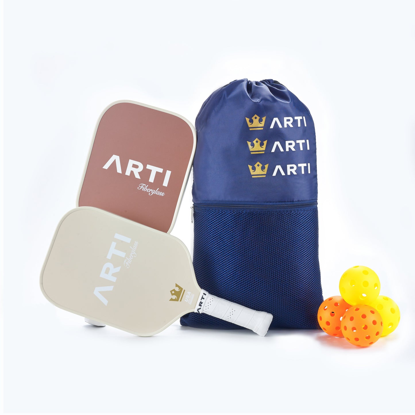 The ARTI Fiberglass "Sandstorm" Pickleball Paddle Set includes two USAPA-approved paddles (brown and white), three yellow balls, and a blue drawstring bag with “ARTI” and gold crown logos plus mesh pockets. White background.