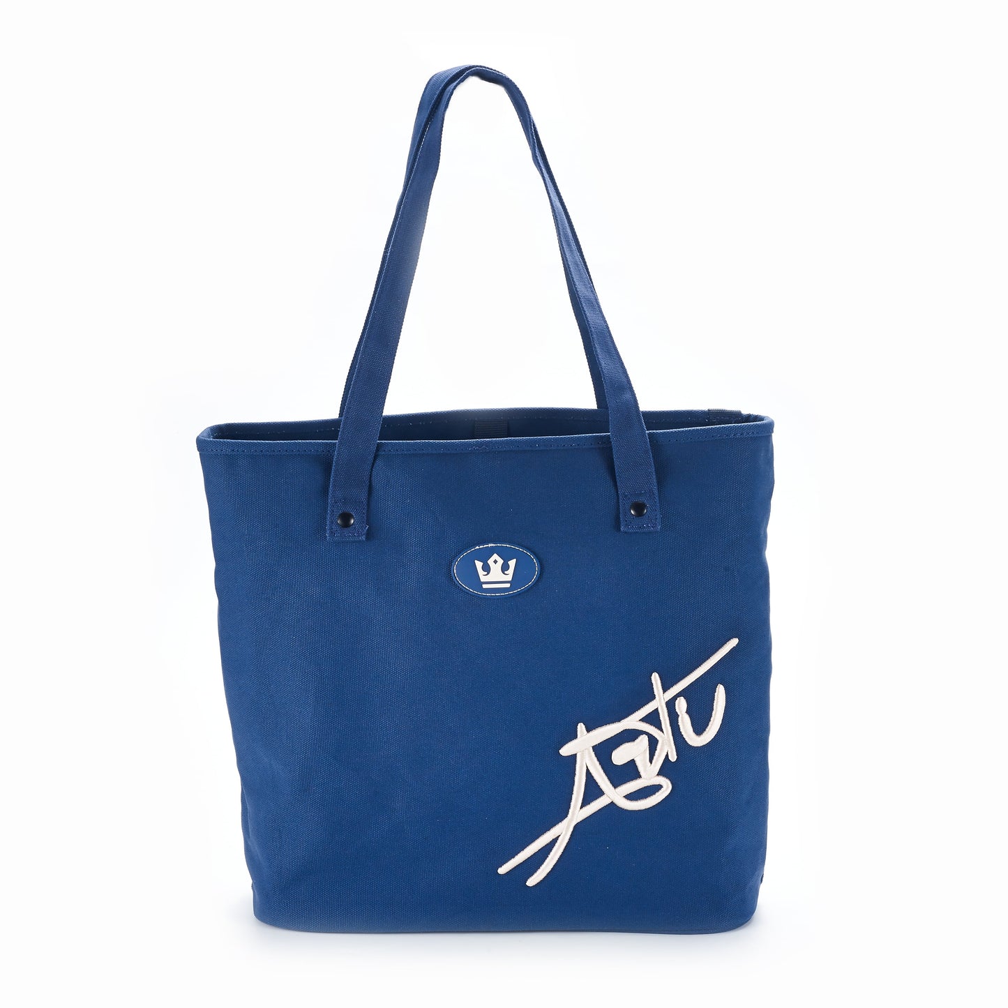 The ARTI Navy Tote Bag by ARTI is an eco-friendly, durable cotton canvas tote with two handles, featuring a white crown emblem at the top center and a large white signature on the lower right corner.
