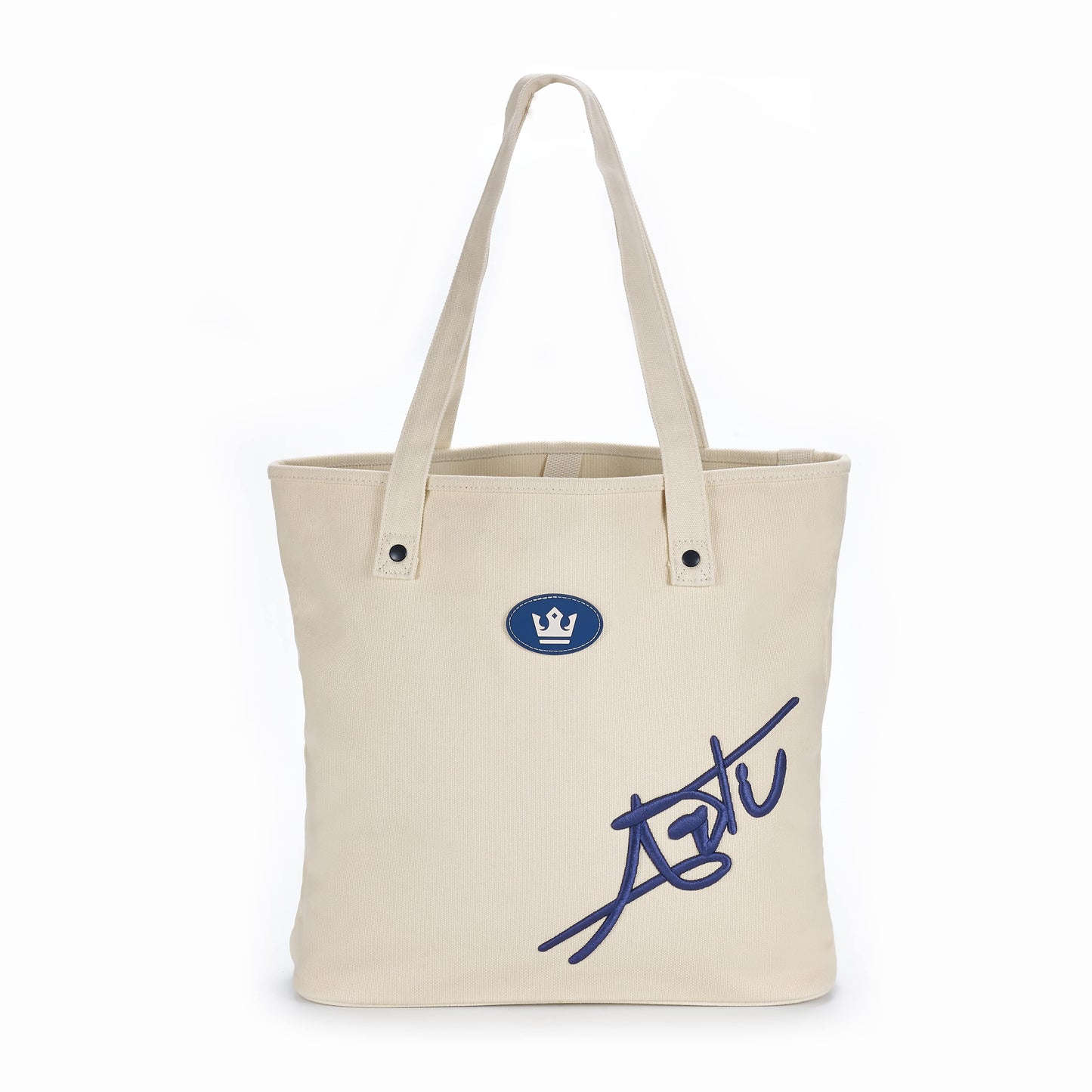 The ARTI Cream Tote Bag by ARTI is a cream cotton bag with two handles, featuring a blue crown emblem near the top center and a large, stylized blue "Astt" signature at the lower right on a plain white background.