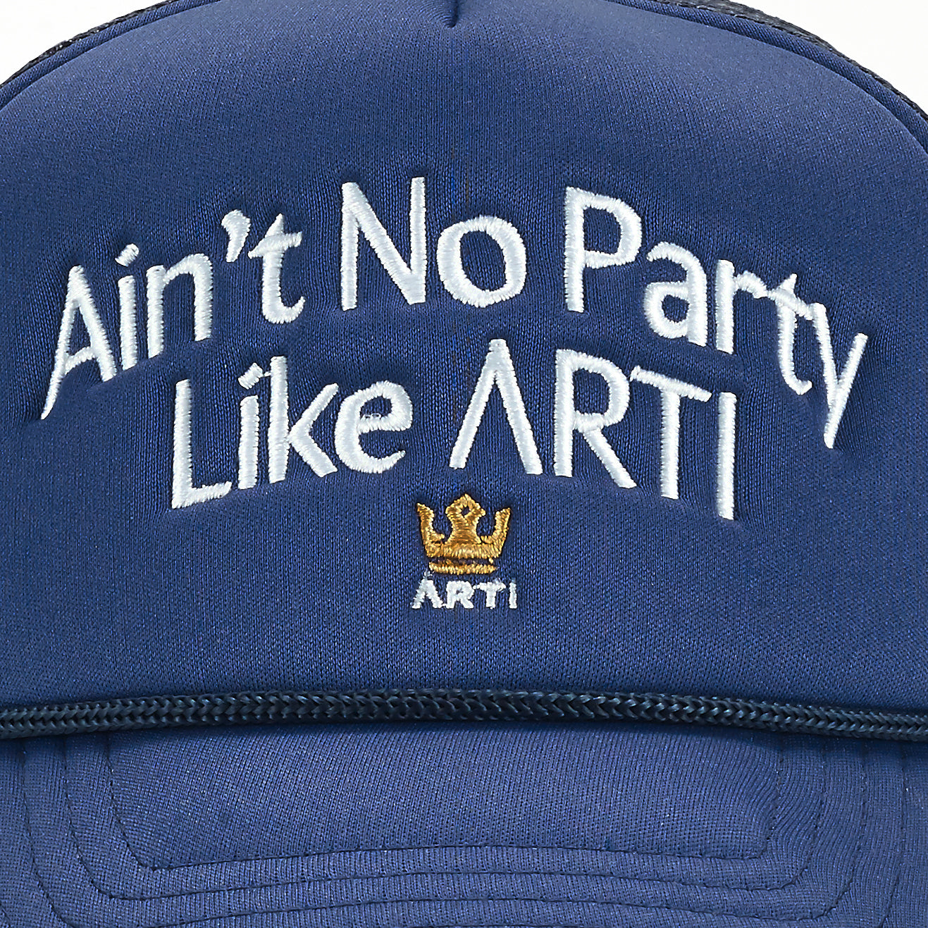 A close-up of the ARTI “Ain’t No Party Like ARTI” Trucker Hat—a navy blue, lightweight sports cap with white embroidered text and a small gold crown above “ARTI.” The brand’s stitching and fabric texture are clearly shown.