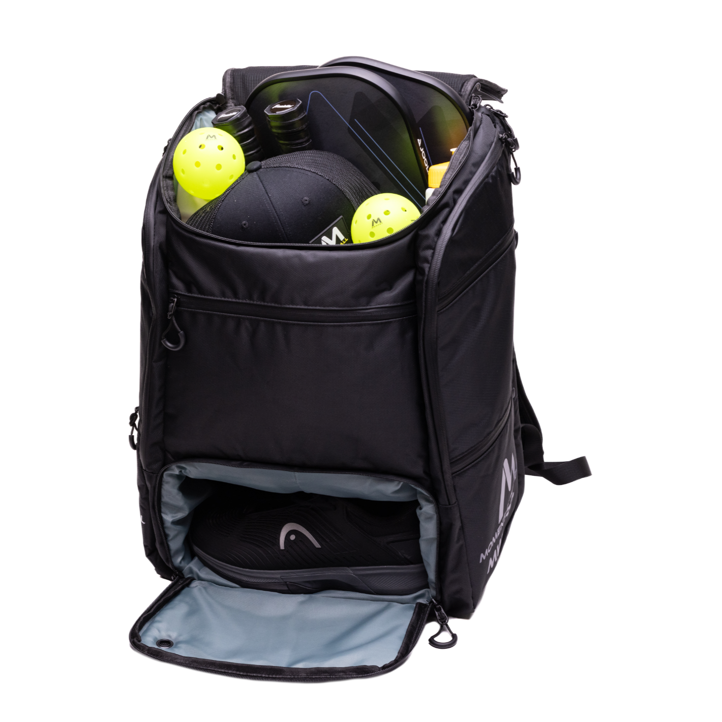 The Moment Pickleball MW-PRO Bag / Travel Bag in Black/Silver stands upright with its main compartment open, displaying two yellow pickleballs, a black cap, sunglasses, and a water bottle. The lower zippered section holds black athletic shoes.