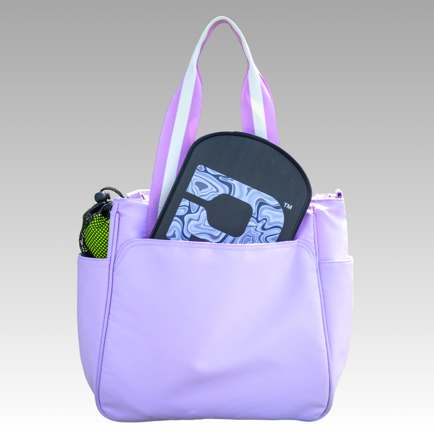 The Playly Store Lulu Pickleball Tote features white and lavender handles, side pockets (including a mesh water bottle holder), and a roomy compartment with a black paddle, making it the perfect pickleball accessory. Set against a smooth gradient background.