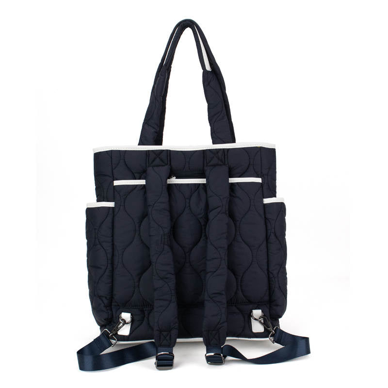 The Fifth Ave Pickleball Convertible Tote Bag/Backpack by Queen of the Court features a black quilted design, navy blue adjustable straps, tote handles, two side pockets, silver hardware, and circular stitching for style and versatility.