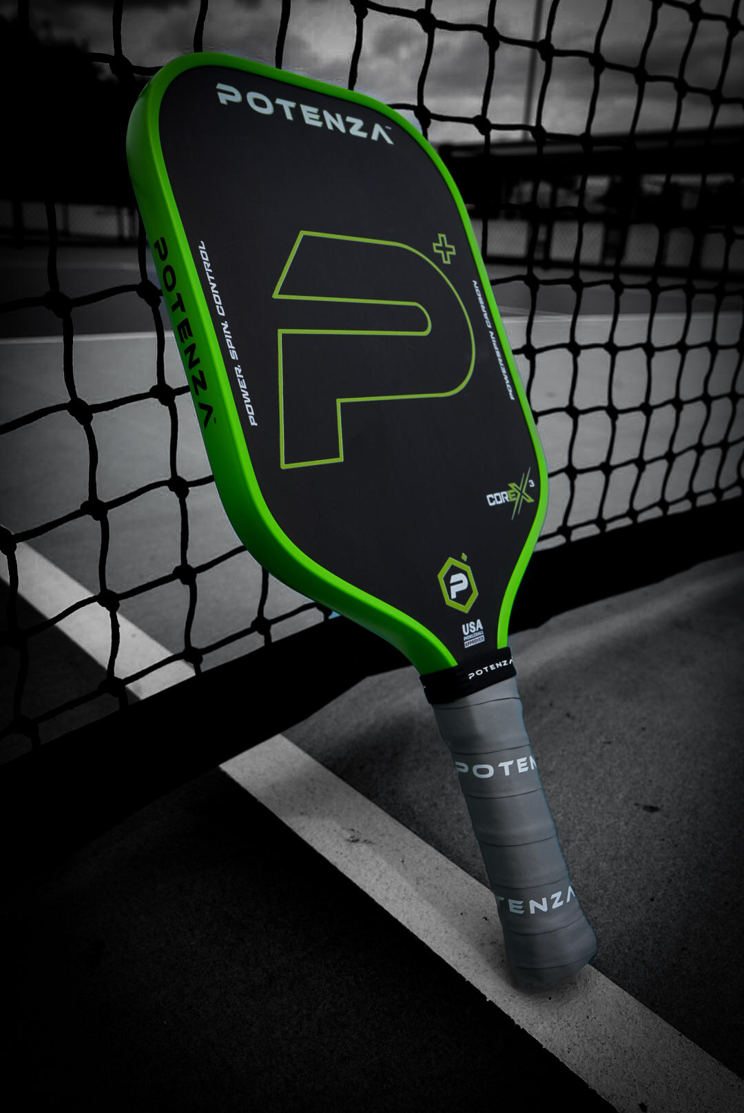 The Potenza Pickleball P+ PowerSpin Carbon COREx3 (Neon Green) paddle, featuring a black face, neon green edges, and the “P” logo, with a gray handle and visible branding, leans against an outdoor tennis net as the background blurs.