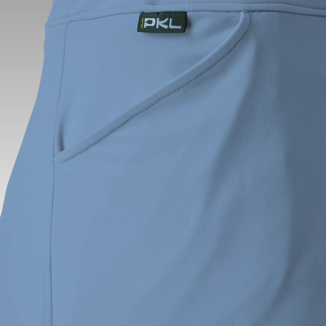 Close-up of the Sammy Skort 2.0 by Playly Store in light blue CoolFlow fabric, featuring a diagonal seam, hip pocket, and green PKL tag on the waistband. Soft gradient background highlights this stylish court-ready skort.