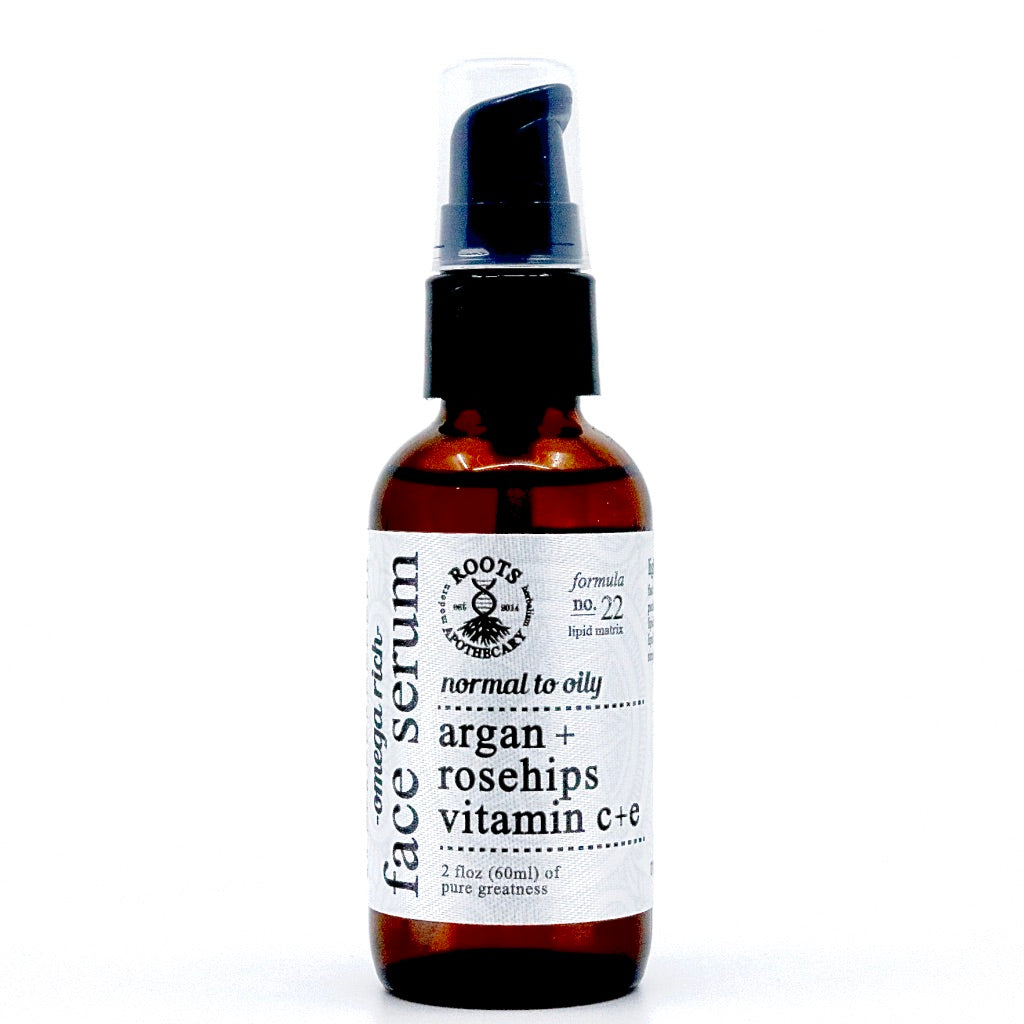 A brown glass bottle with black pump labeled "Roots Apothecary face serum" features unrefined argan oil and vitamins C+E for antioxidant benefits, ideal for normal to oily skin in a sleek 2 oz (60ml) black and white design.